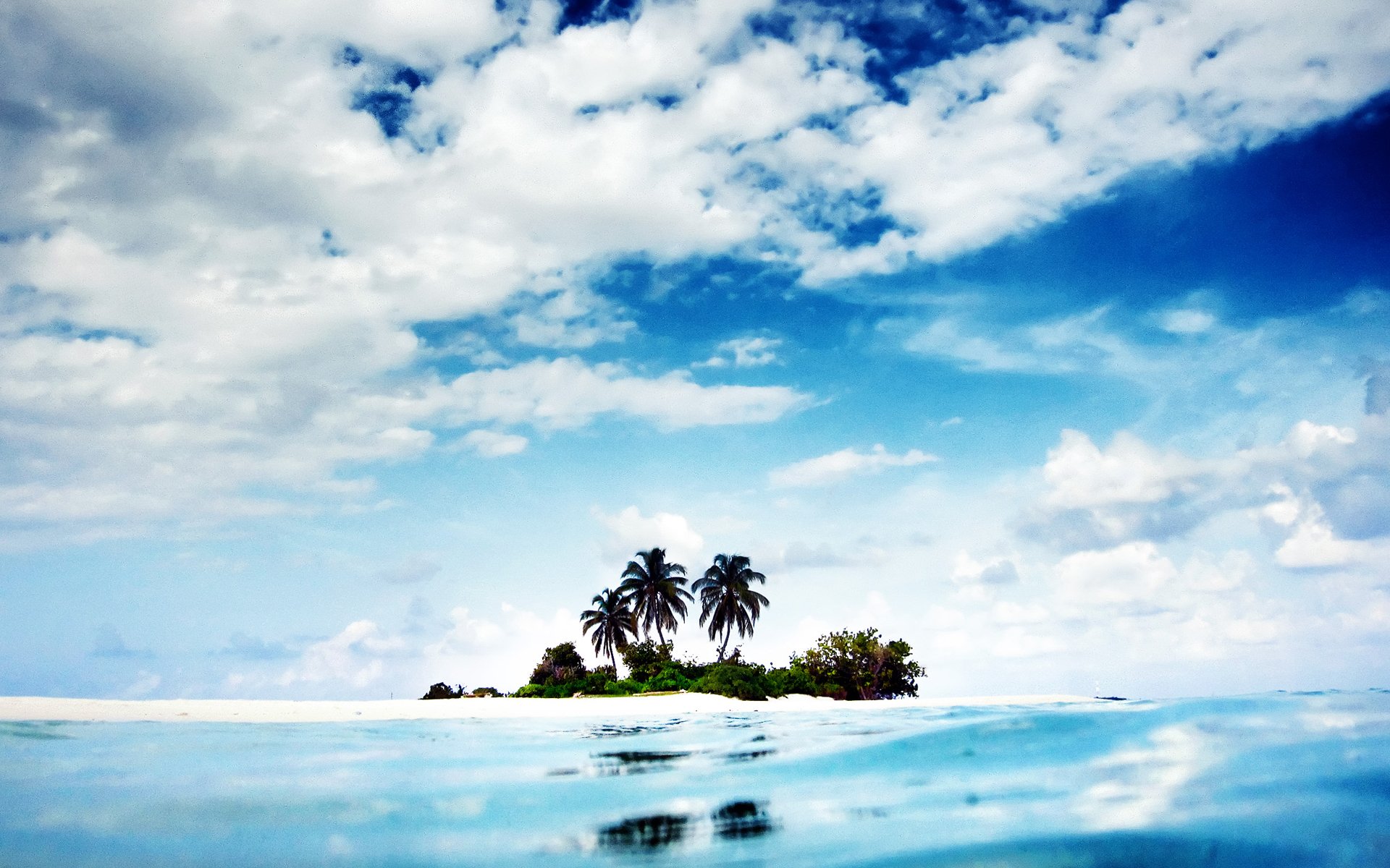 A serene tropical island with palm trees rises amidst calm blue waters, under a bright sky filled with fluffy white clouds, capturing the essence of nature's beauty.
