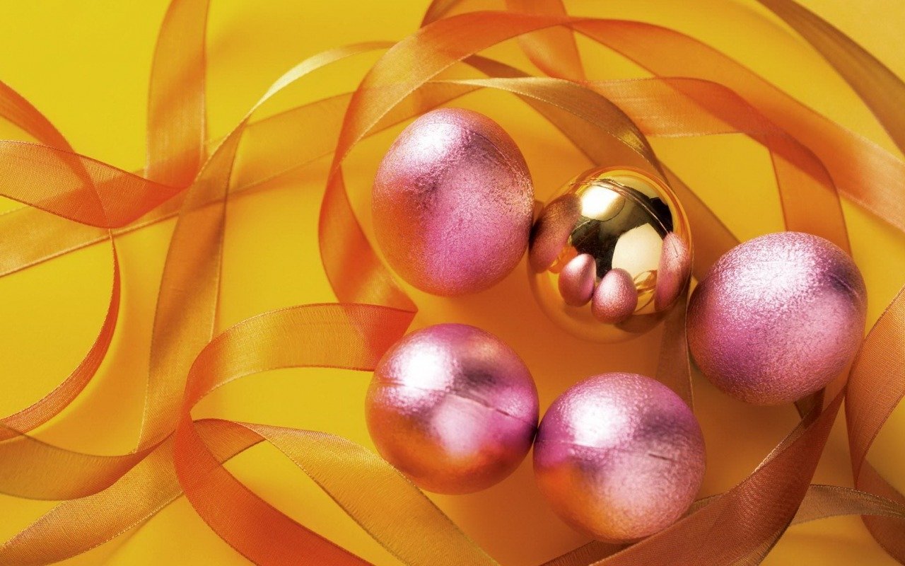A collection of pink and gold Christmas ornaments surrounded by shiny orange ribbons against a yellow background, evoking a festive holiday atmosphere.