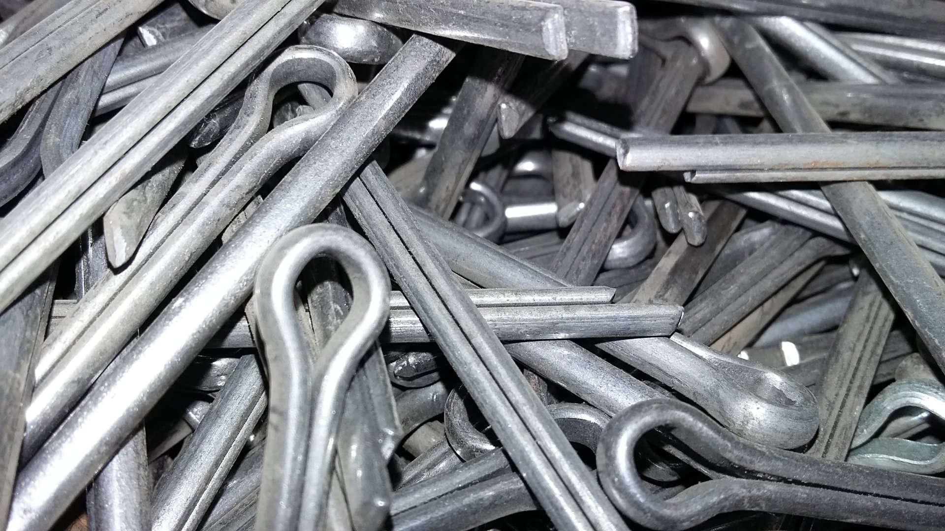 Close-up photography of numerous metallic cotter pins piled together, showcasing their looped heads and straight shafts.