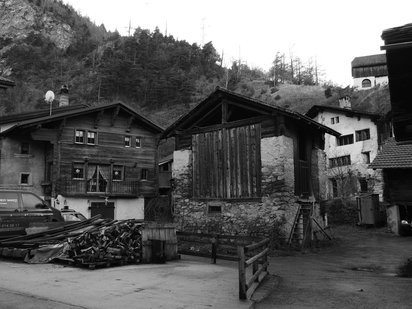 A scenic black-and-white image of rustic man-made houses nestled against a mountainous backdrop, showcasing a mix of wooden and stone structures.
