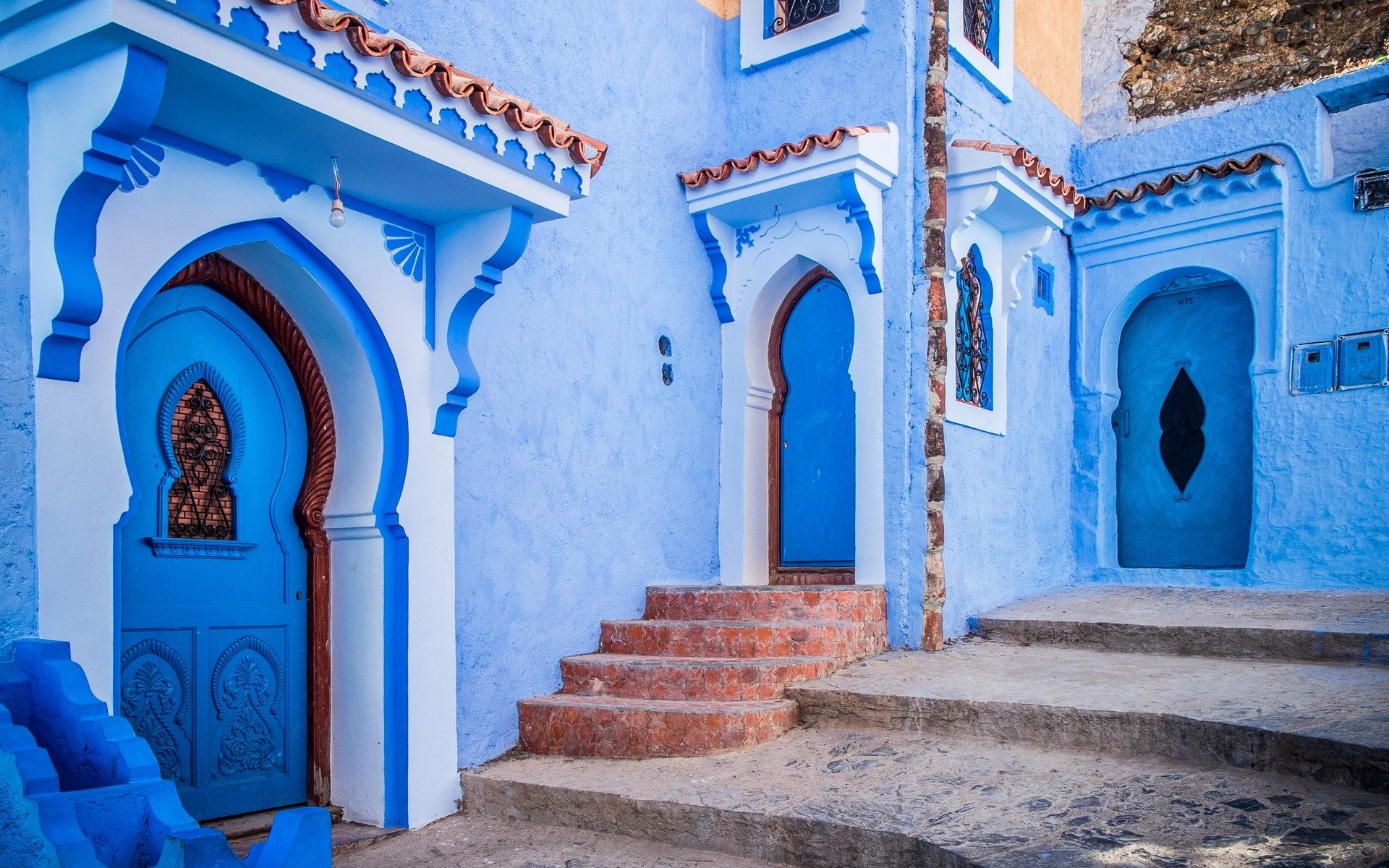Bright blue man-made house with arched doorways and terracotta steps in Santorini, showcasing traditional Mediterranean architecture.