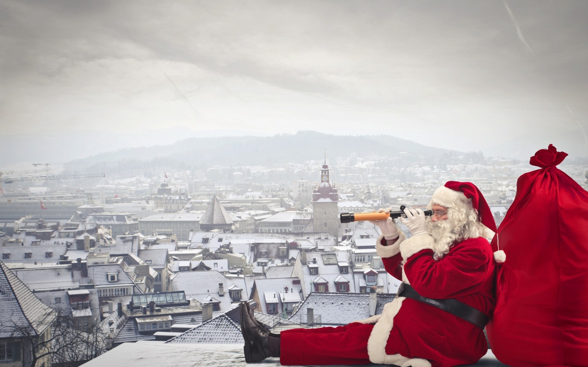 Santa Claus dressed in red enjoys a drink while sitting on a snowy rooftop, with a large red sack beside him and a cityscape in the background during the holiday season.