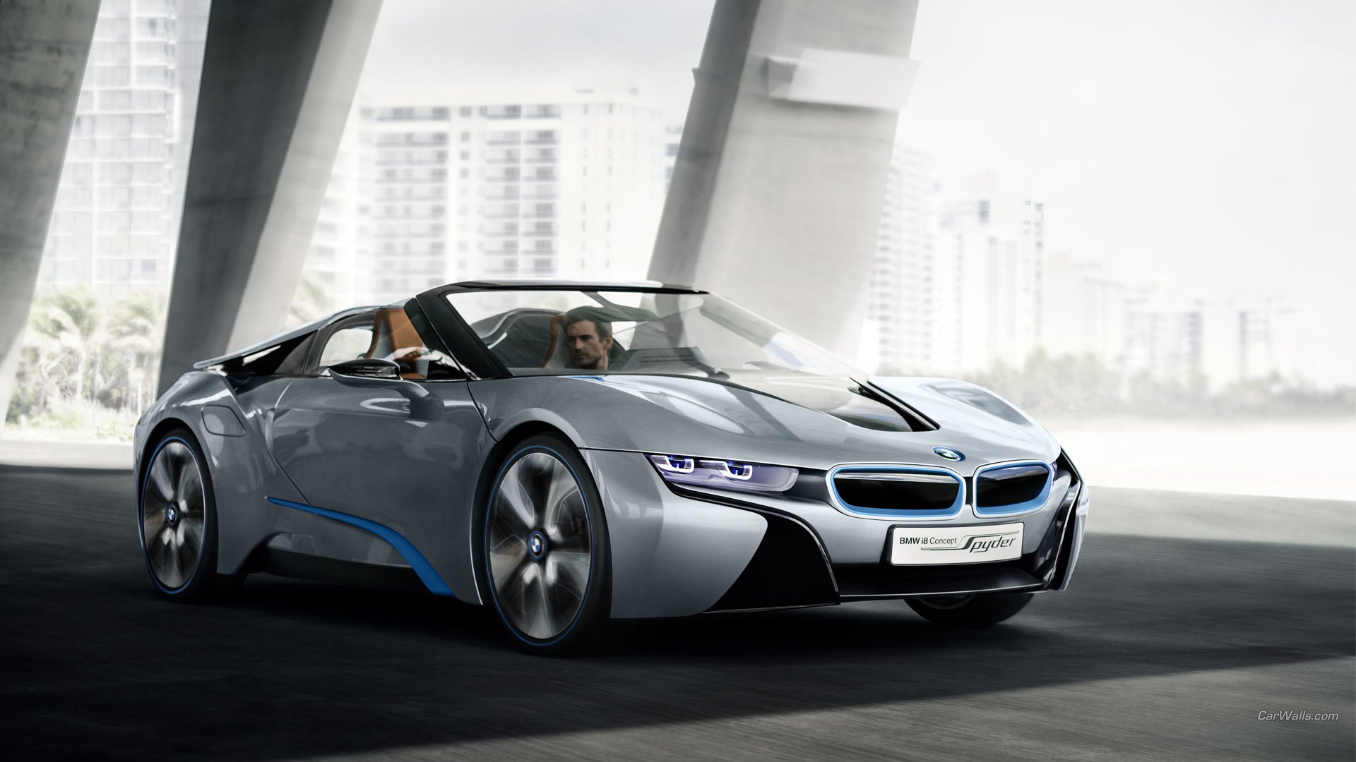 Sleek silver BMW i8 Concept Spyder convertible displayed in a modern urban setting with dynamic lighting highlighting its aerodynamic design.
