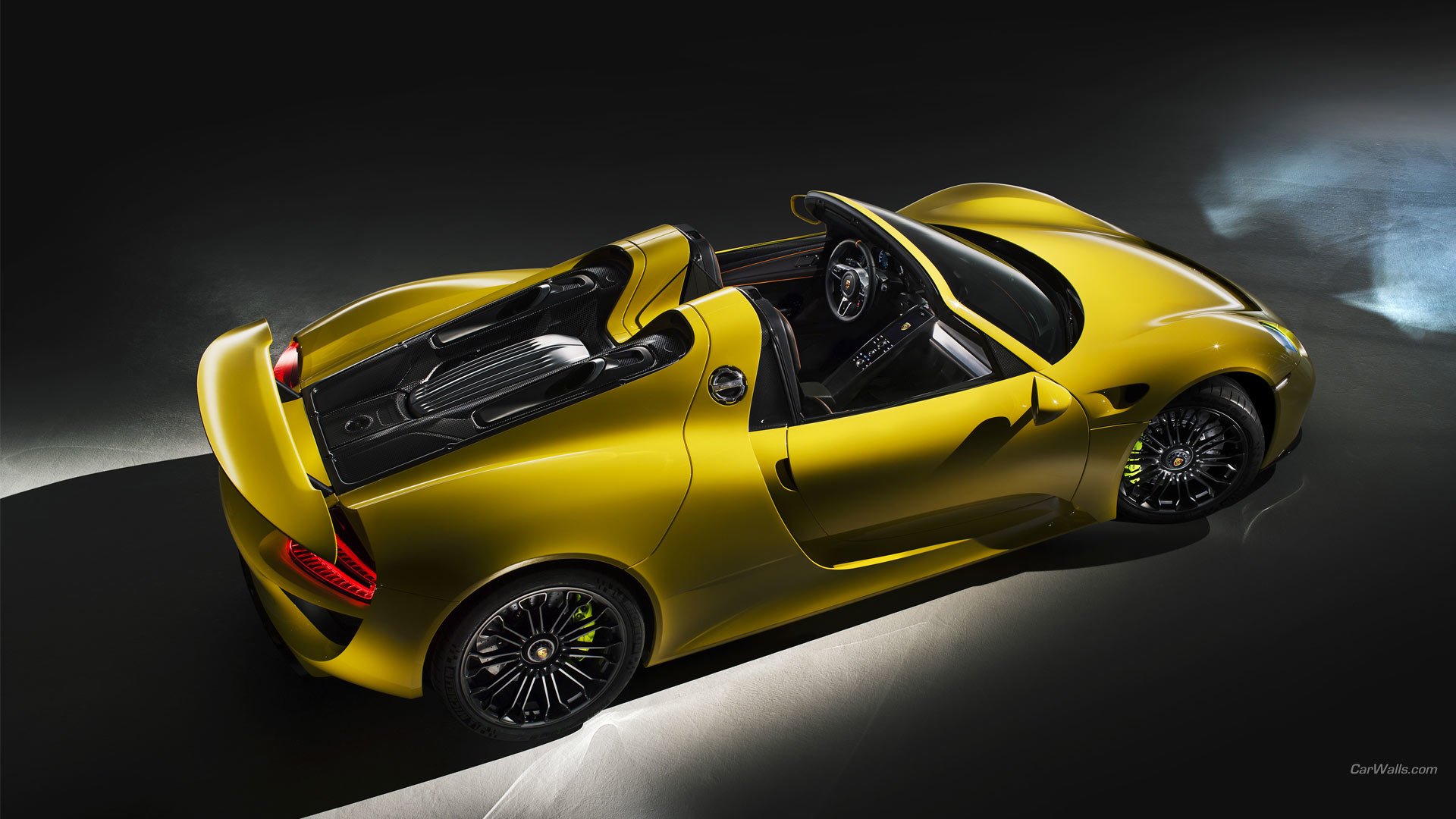 A striking yellow Porsche 918 Spyder showcased from an overhead angle, highlighting its sleek design and convertible features against a dramatic dark background.