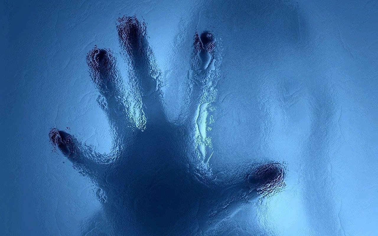 Photographic close-up of a hand pressed against frosted glass, fingers splayed and backlit by blue light.