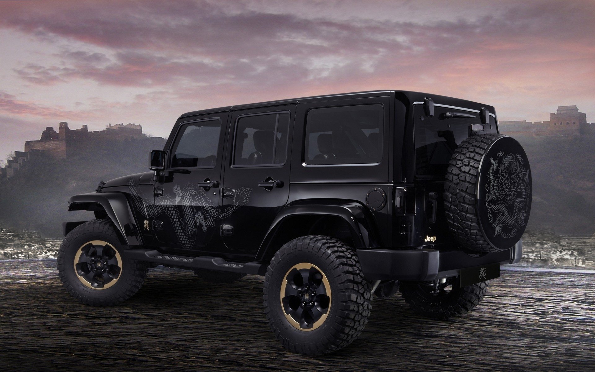 Black Jeep vehicle parked on a rugged terrain with a scenic sunset and cityscape in the background.