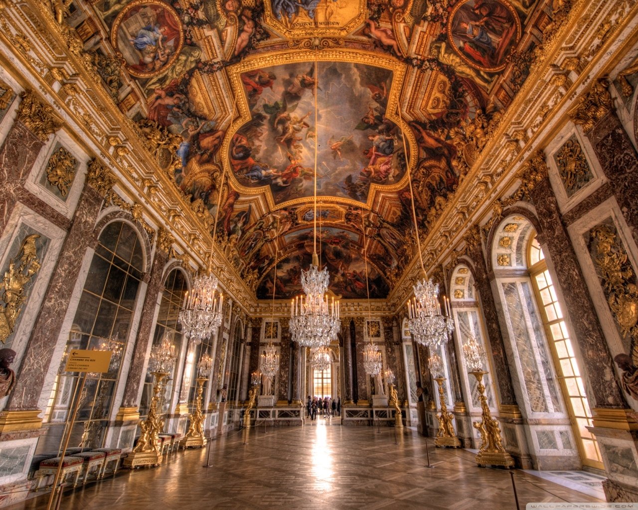 HDR interior view of the gilded, man-made architecture of the Palace of Versailles grand hall with painted vaulted ceiling and crystal chandeliers.