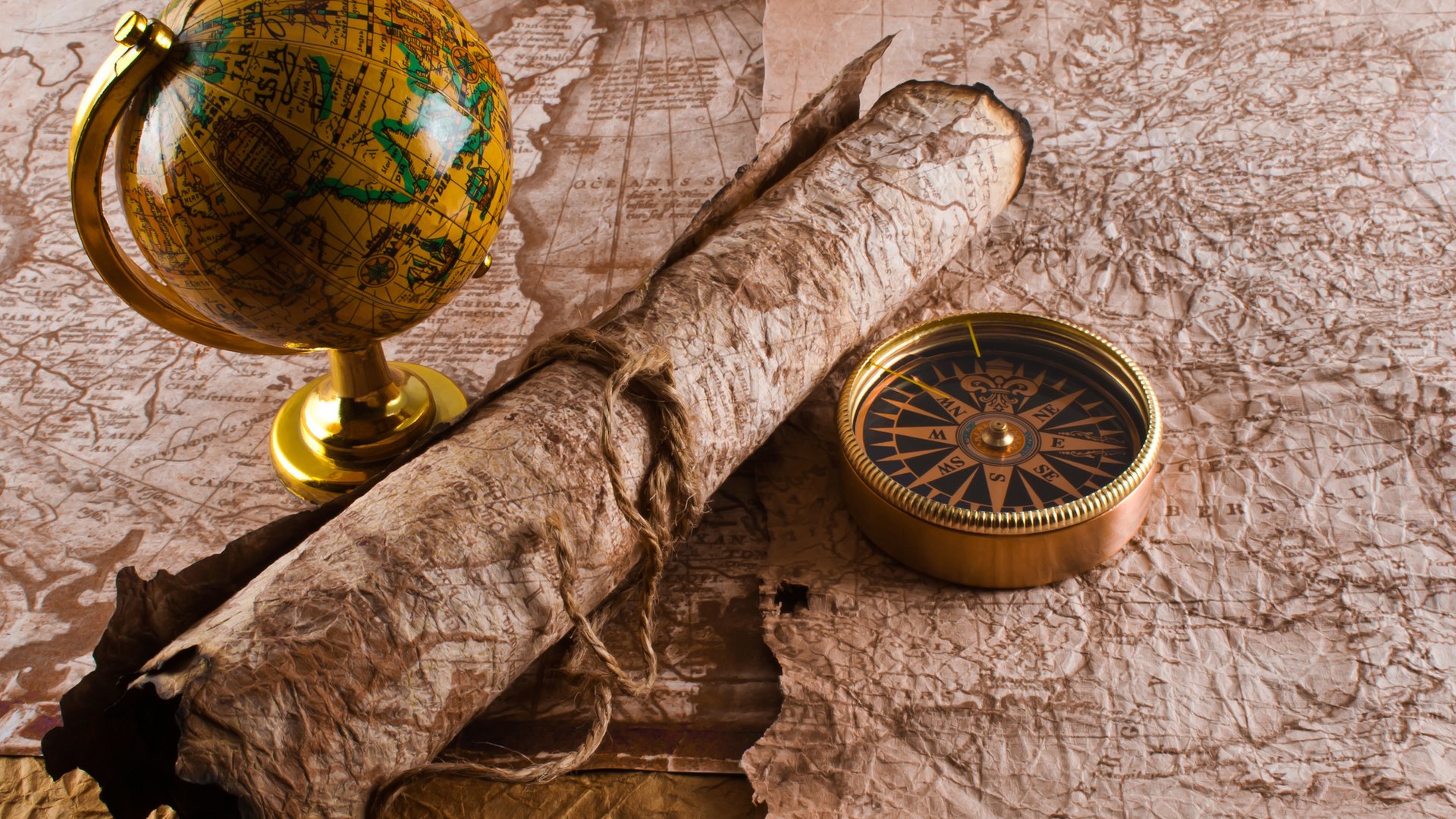 A vintage map laid out with an old globe, a rolled parchment tied with string, and a brass compass, capturing a classic exploration theme. Misc,map.