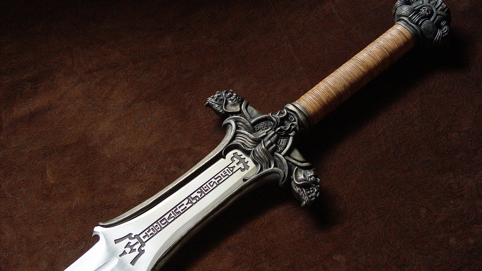A detailed man-made sword with an ornate handle and decorative crossguard, resting on a rich brown surface, showcasing craftsmanship and design.