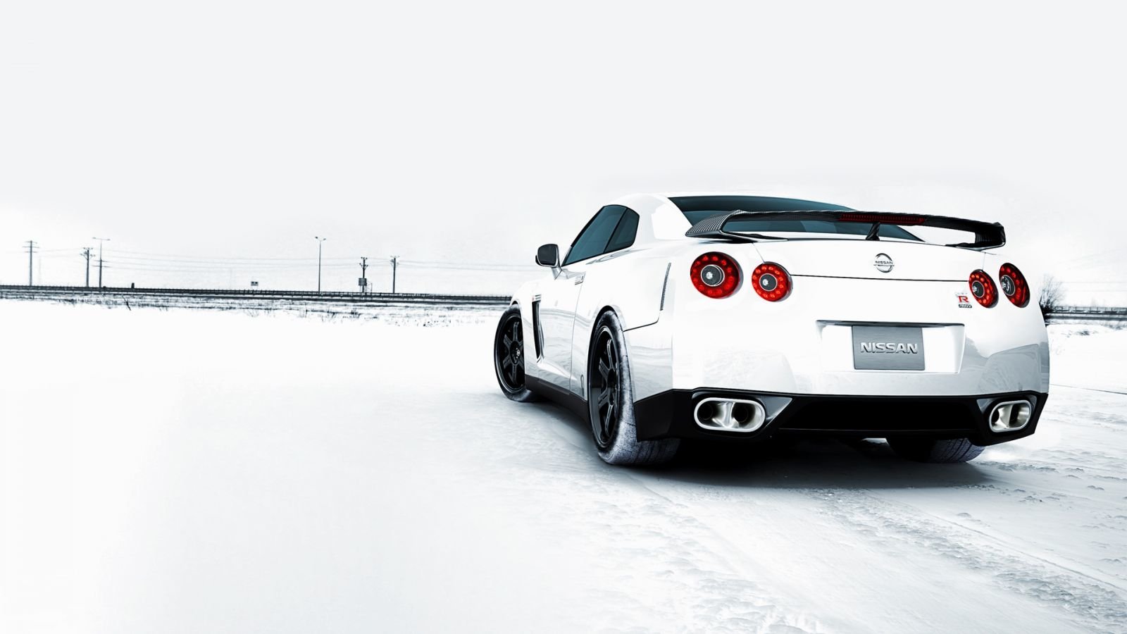A sleek white Nissan sports car is parked on a snowy landscape, showcasing its stylish design and sporty rear features against a minimalist winter backdrop.