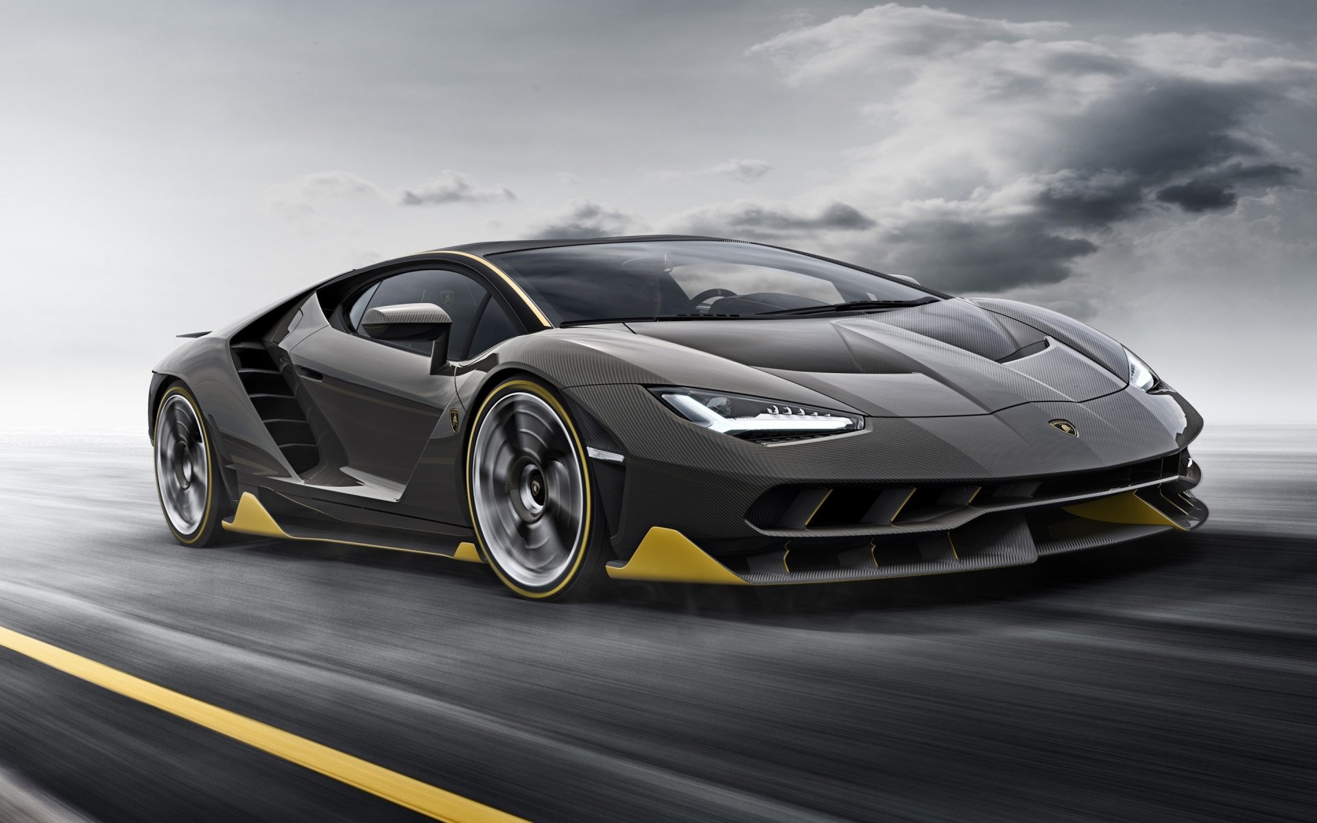 A sleek black Lamborghini Centenario speeds on a wet road under a cloudy sky, showcasing its sharp design and aerodynamic features.