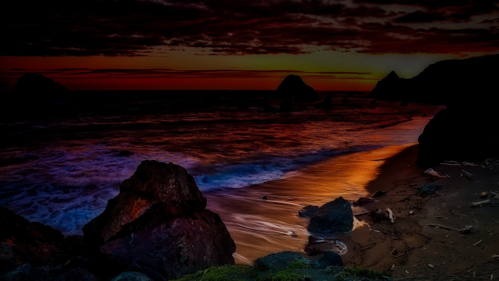 HDR sunset over a rocky coastline and ocean, waves washing glowing sky reflections onto a sandy beach — a tranquil nature scene.