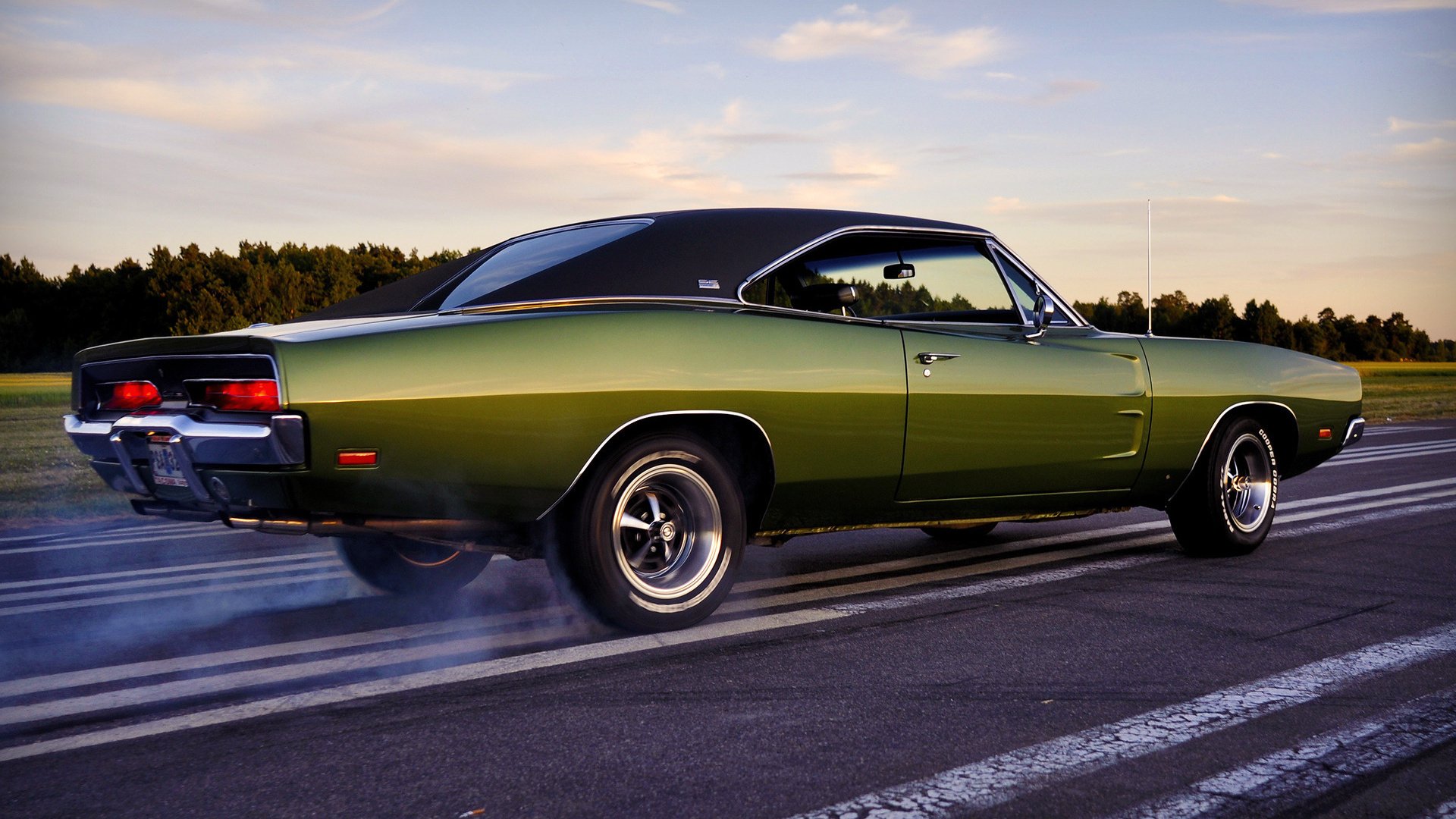 Green Dodge Charger vehicle drifting on a runway, rear tires smoking beneath a sunset sky.