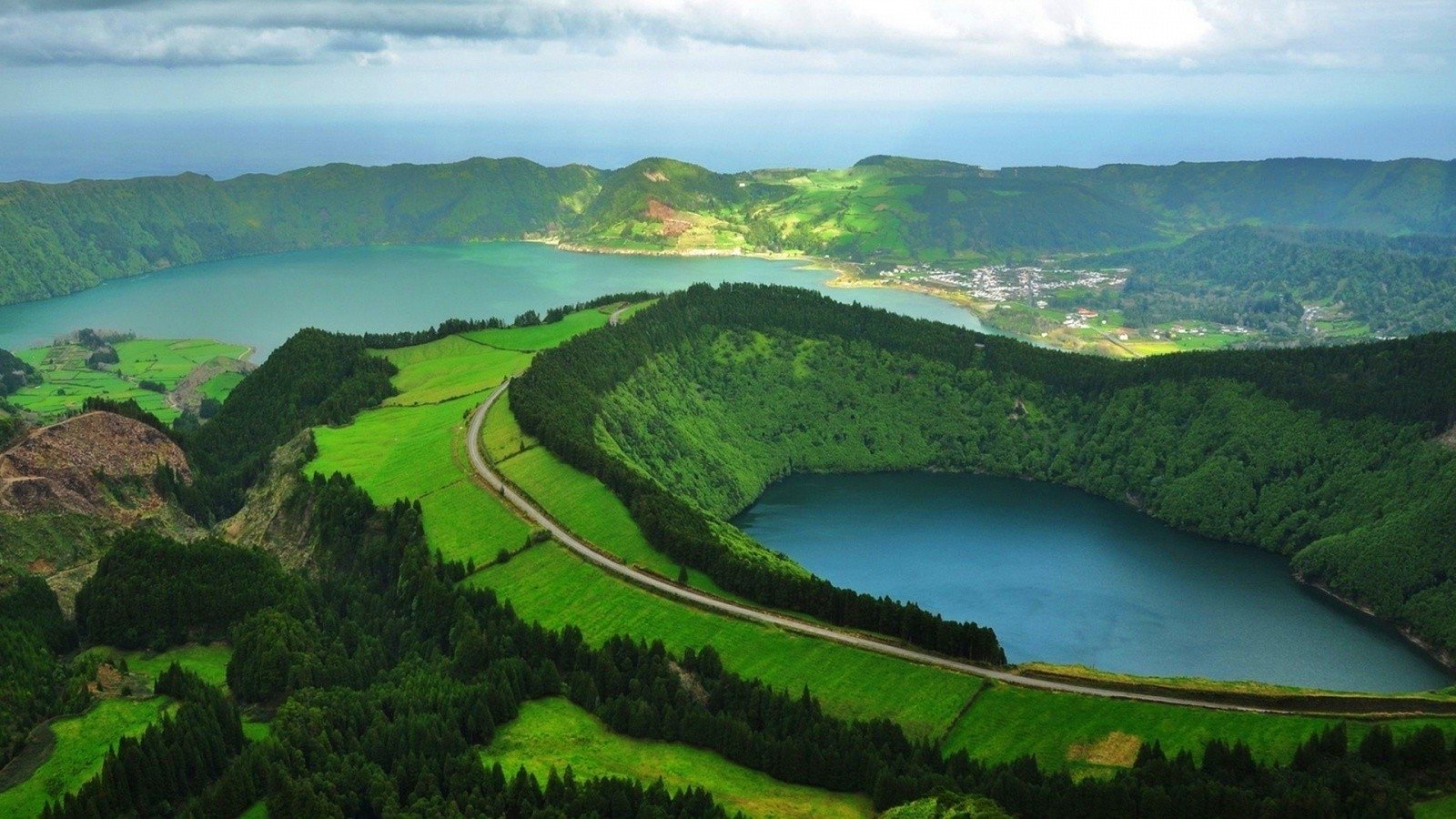 A breathtaking landscape in São Miguel, Portugal, showcasing a serene lake surrounded by lush greenery and mountains under a dramatic sky.