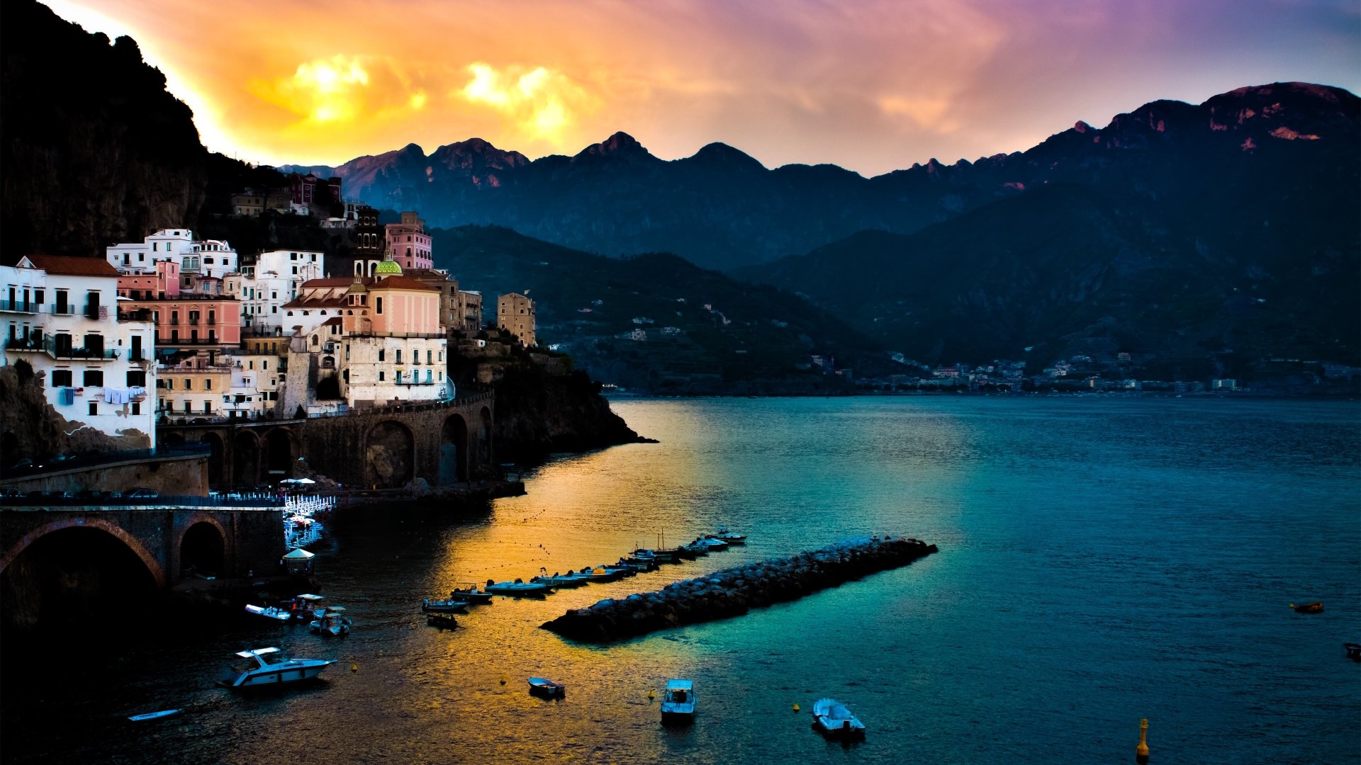 A vibrant coastline at sunset with colorful buildings perched on cliffs and boats floating on calm water, captured in striking photography.