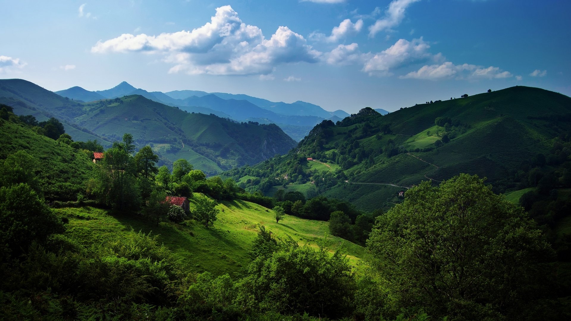 A stunning landscape photograph showcasing lush green hills under a blue sky, with distant mountains and scattered clouds creating a serene and picturesque scene.