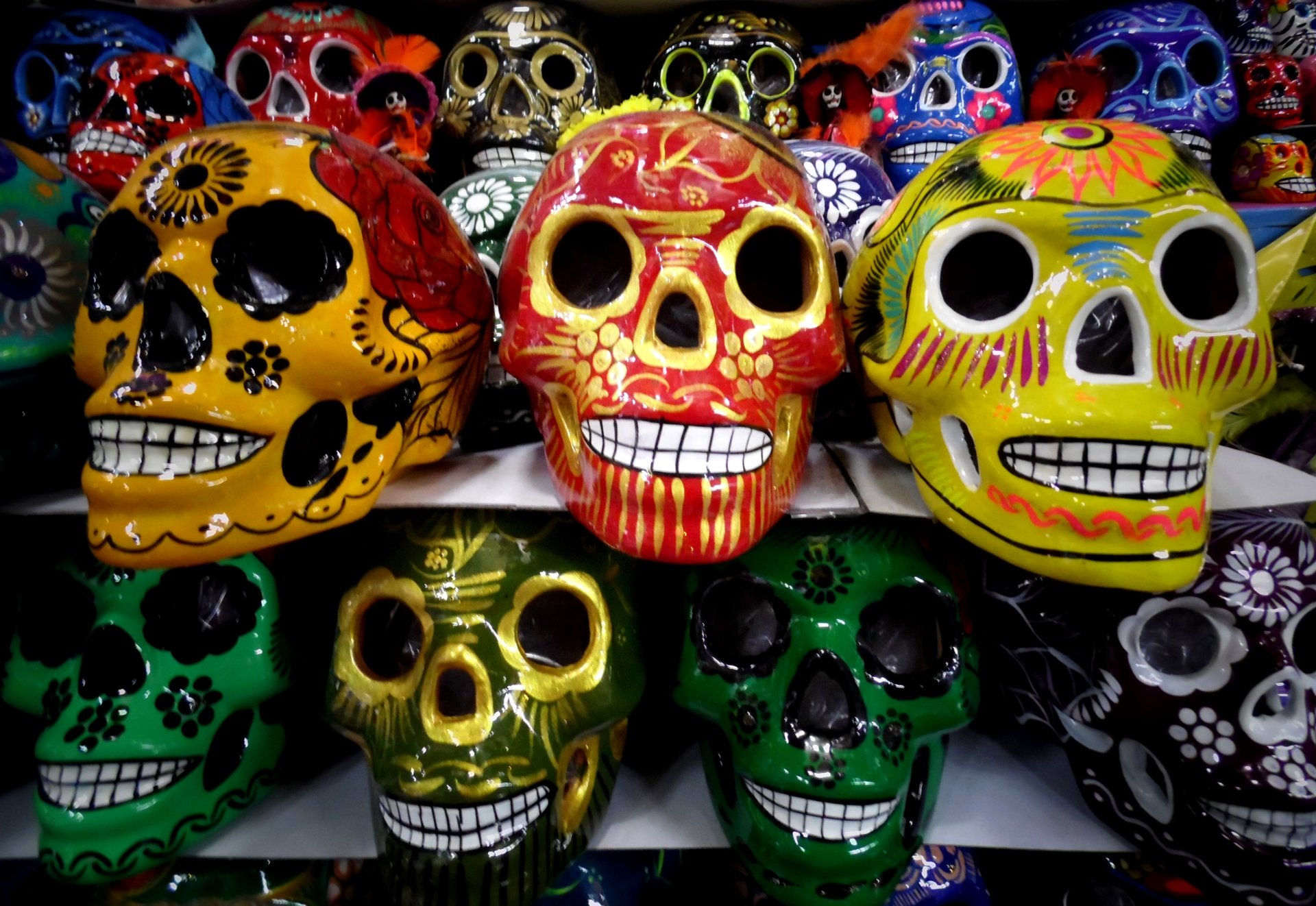Rows of colorful Day of the Dead skulls with painted floral patterns set against a dark backdrop.