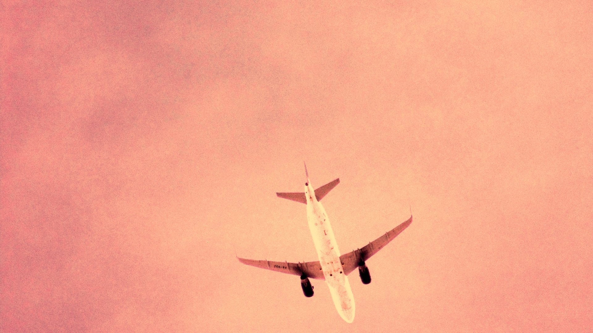 A commercial aircraft vehicle seen from below as it flies across a pink-hued sky.