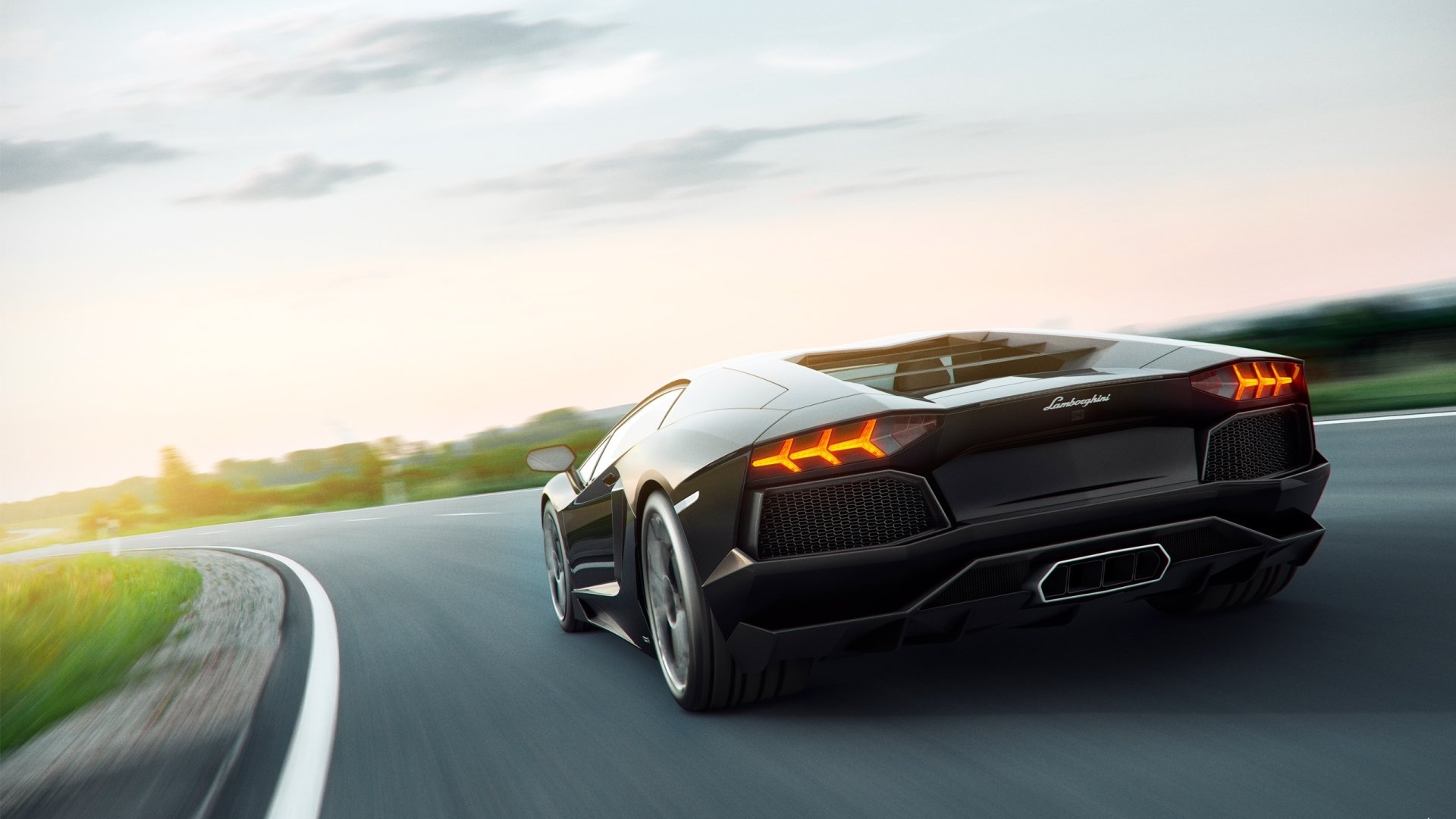A sleek black Lamborghini Aventador accelerates along a winding road as the sun sets, showcasing its powerful design and performance.