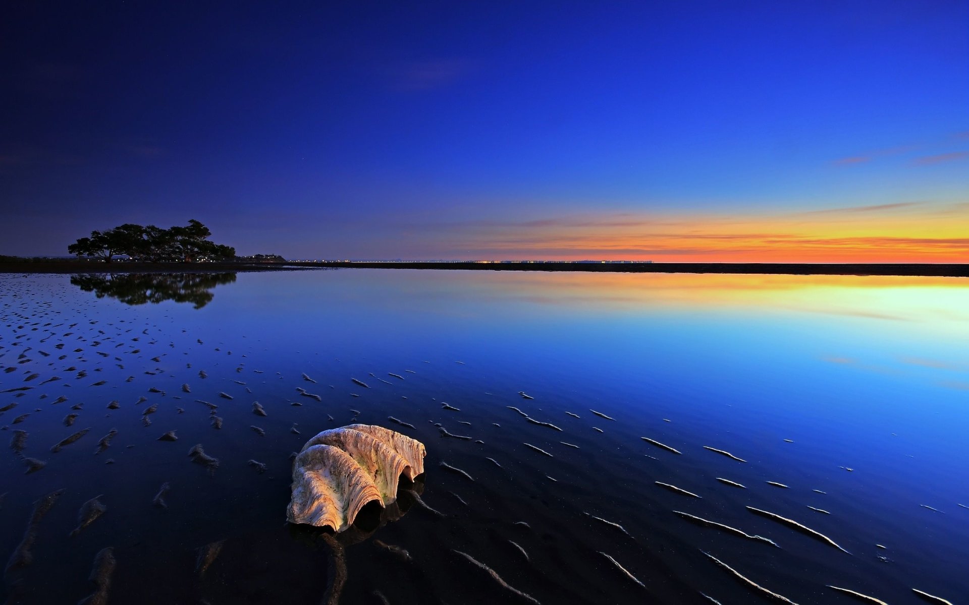 A serene nature scene at sunset with a calm body of water reflecting the vibrant sky and a distant island, creating a peaceful and mirrored landscape.