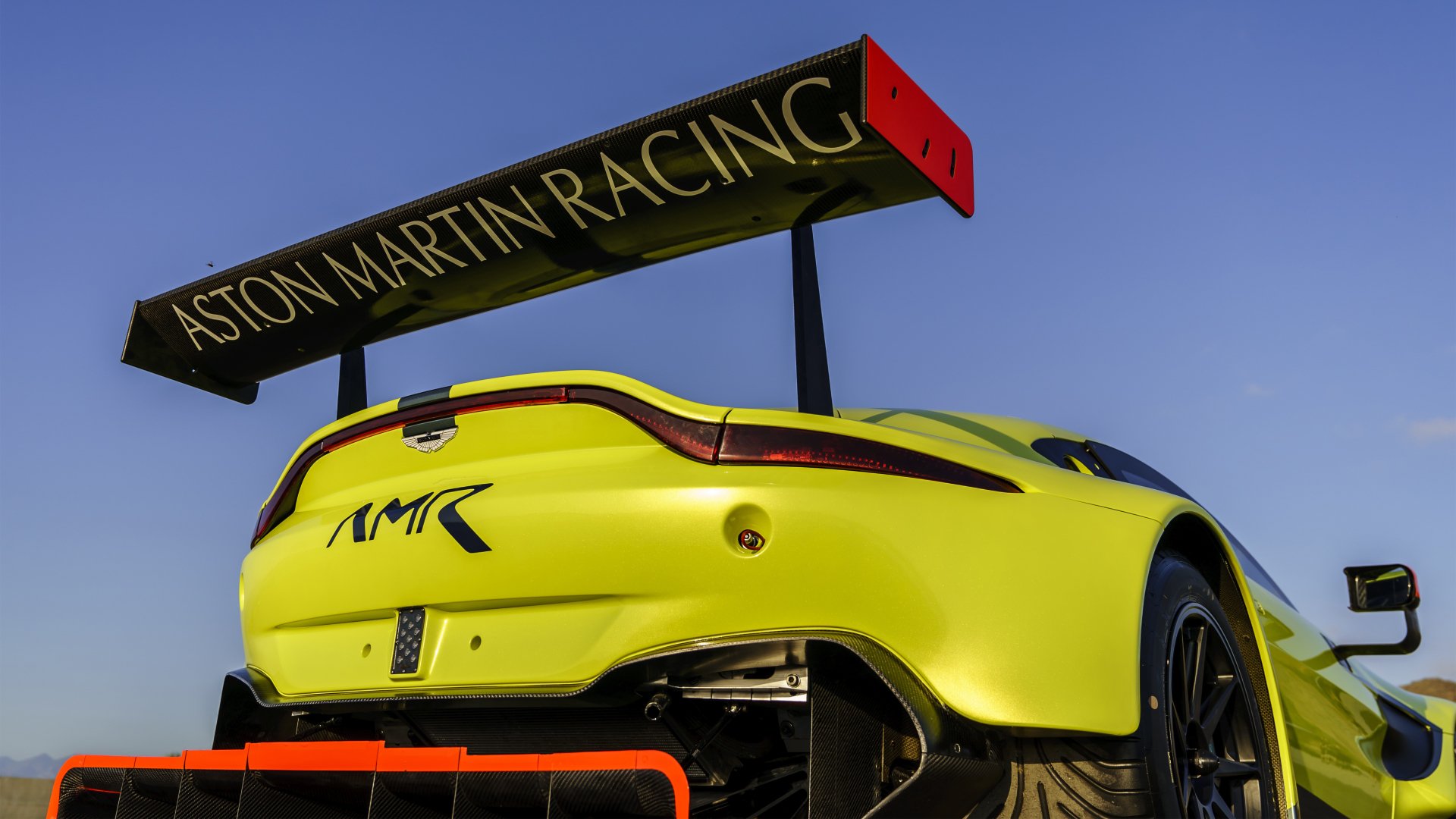 Bright yellow Aston Martin Vantage GTE race car with prominent rear wing and racing decals against a clear blue sky.