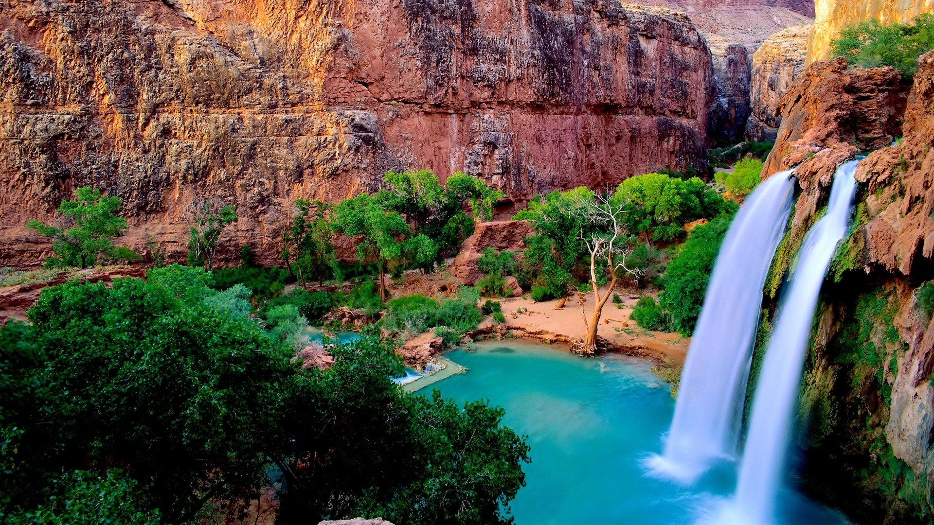 A vibrant nature scene featuring a waterfall cascading into a turquoise pool surrounded by lush greenery and rocky cliffs.