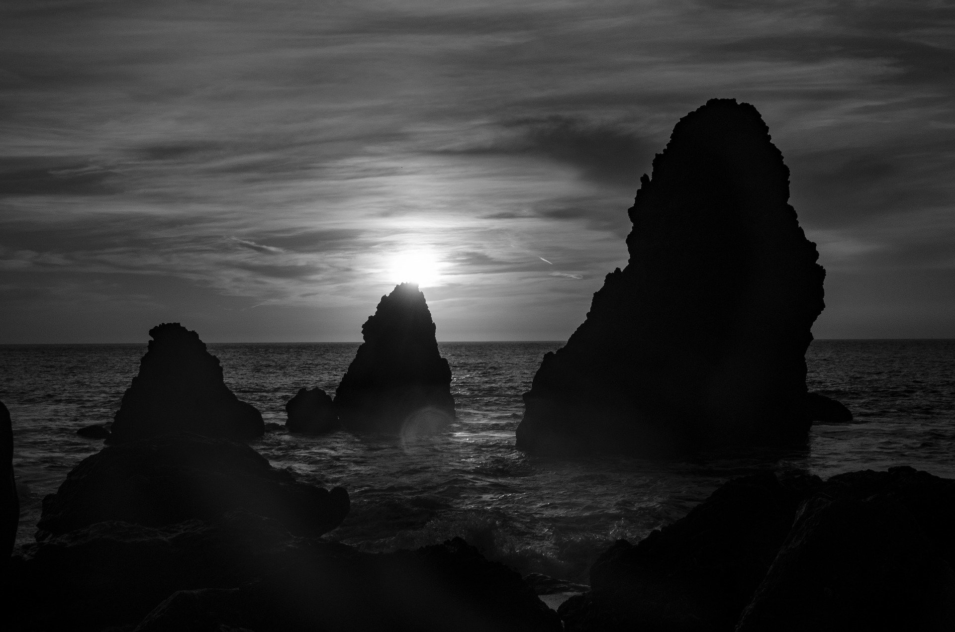 Black and white photograph of ocean rocks silhouetted against a dramatic sunset sky.