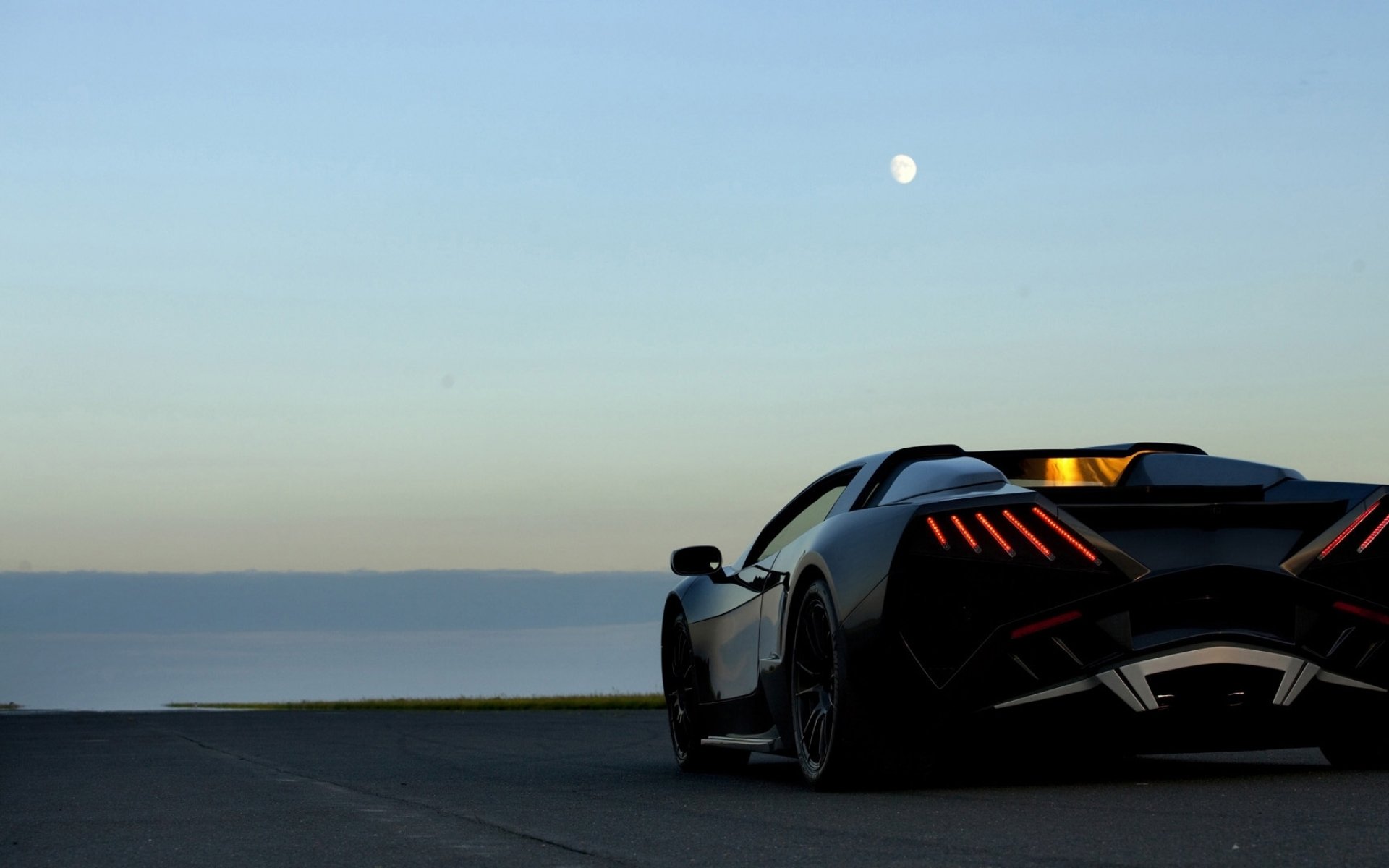 Rear three-quarter view of an Arrinera Veno sports car parked by the waterfront at dusk, moon visible above the horizon.