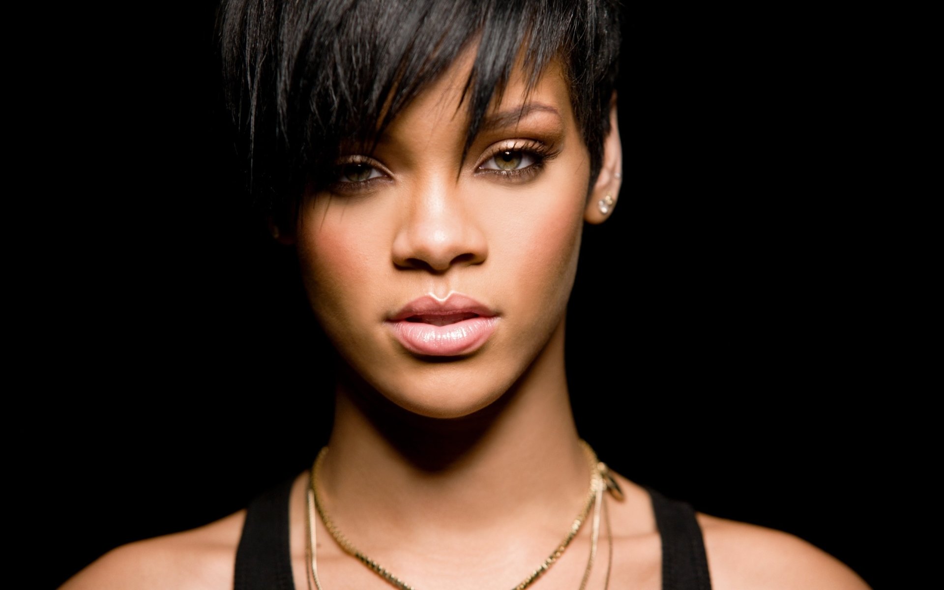 Close-up portrait of Rihanna against a black background, highlighting her confident expression and signature style in the music industry.