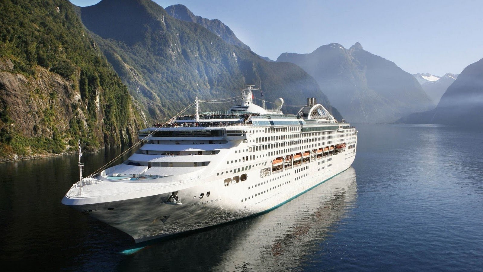 The Sun Princess cruise ship navigates through serene waters, flanked by majestic mountains, showcasing its impressive design and tranquil setting.