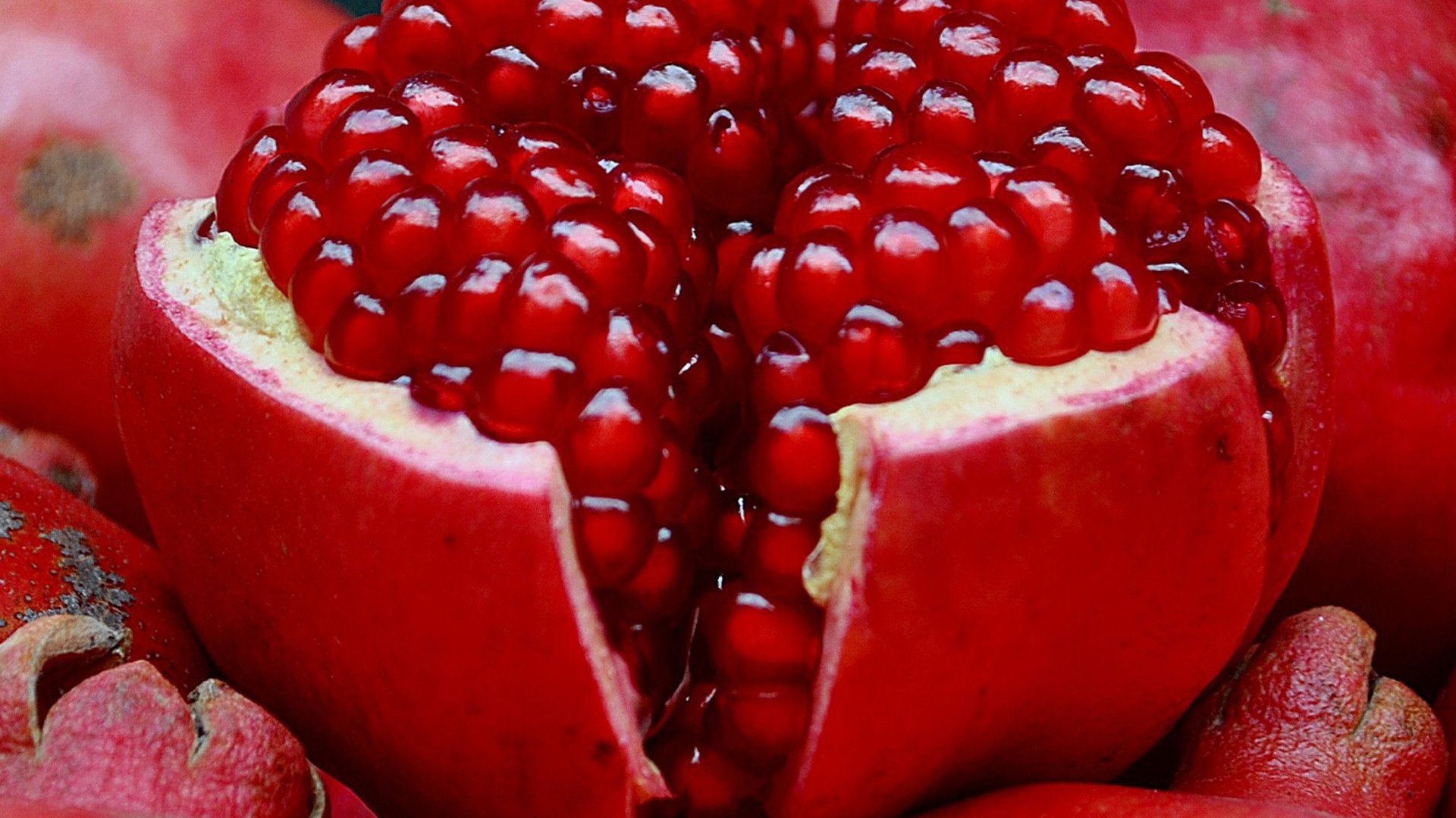 Close-up of a vibrant red pomegranate with its juicy seeds exposed, surrounded by whole pomegranates.