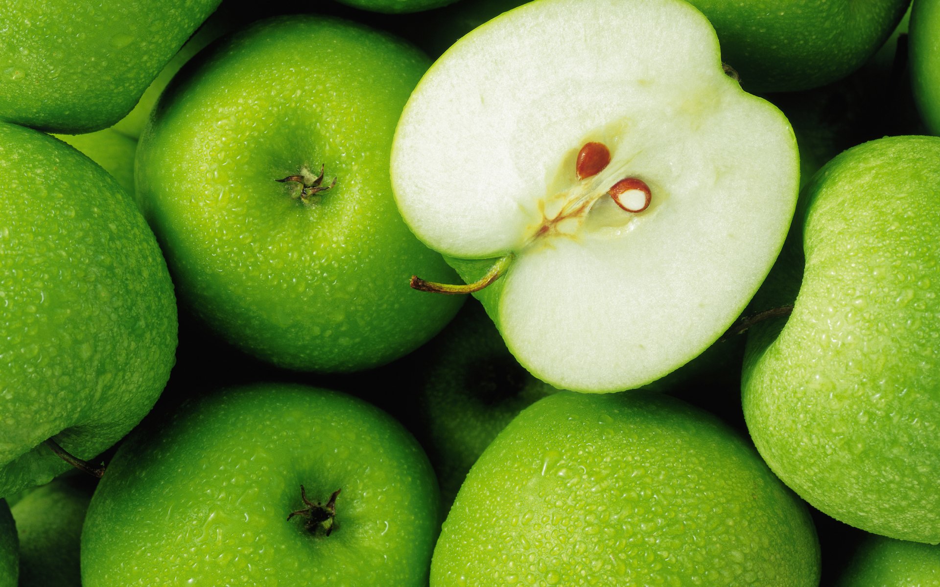 A pile of vibrant green apples, featuring one apple cut in half to reveal its juicy interior and seeds, showcasing the freshness of this delicious food.