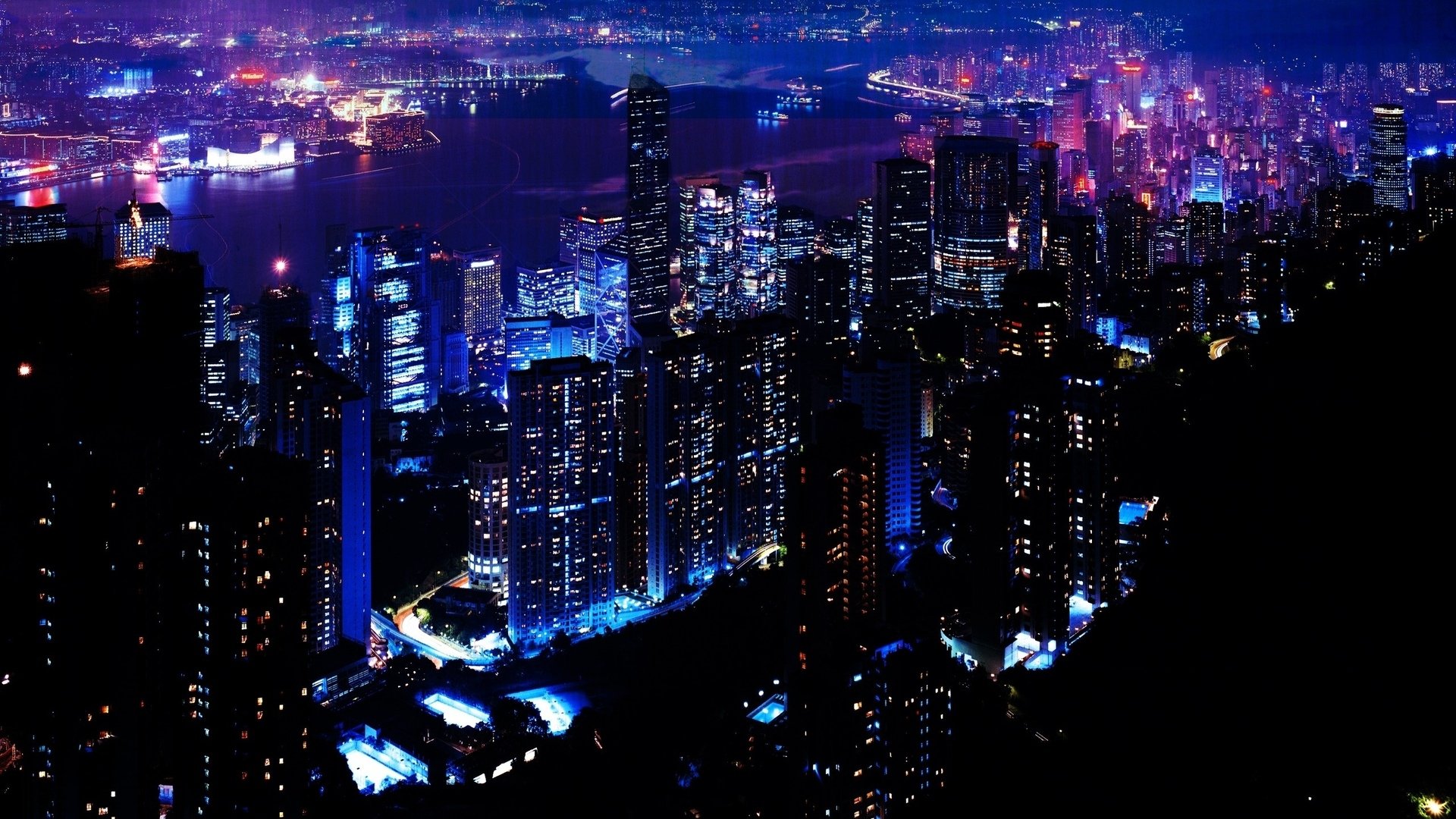 A nighttime aerial view of Hong Kong’s man-made cityscape illuminated by vibrant lights across numerous skyscrapers and surrounding waters.