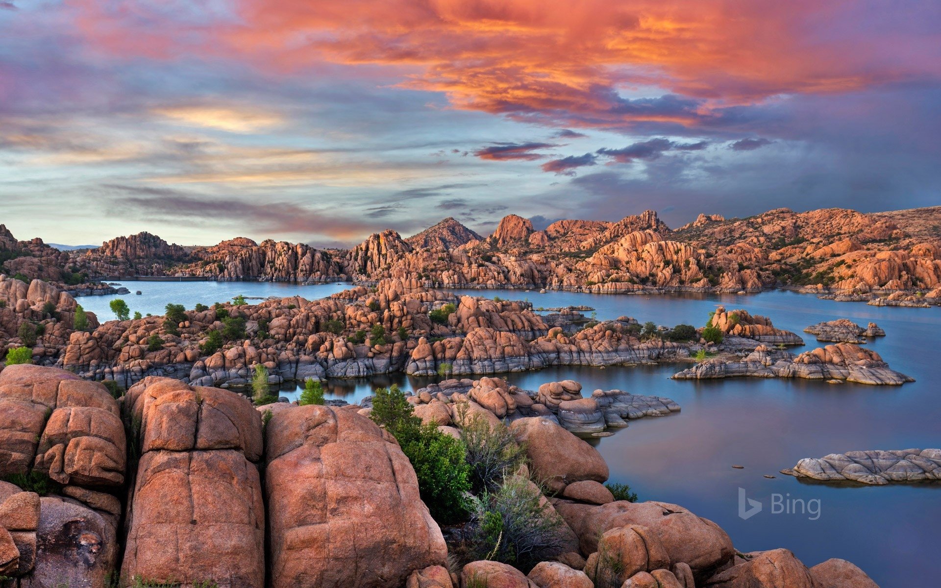Sunset over Watson Lake and the Granite Dells in Arizona, rugged granite islands reflected in the calm lake under a colorful sky.