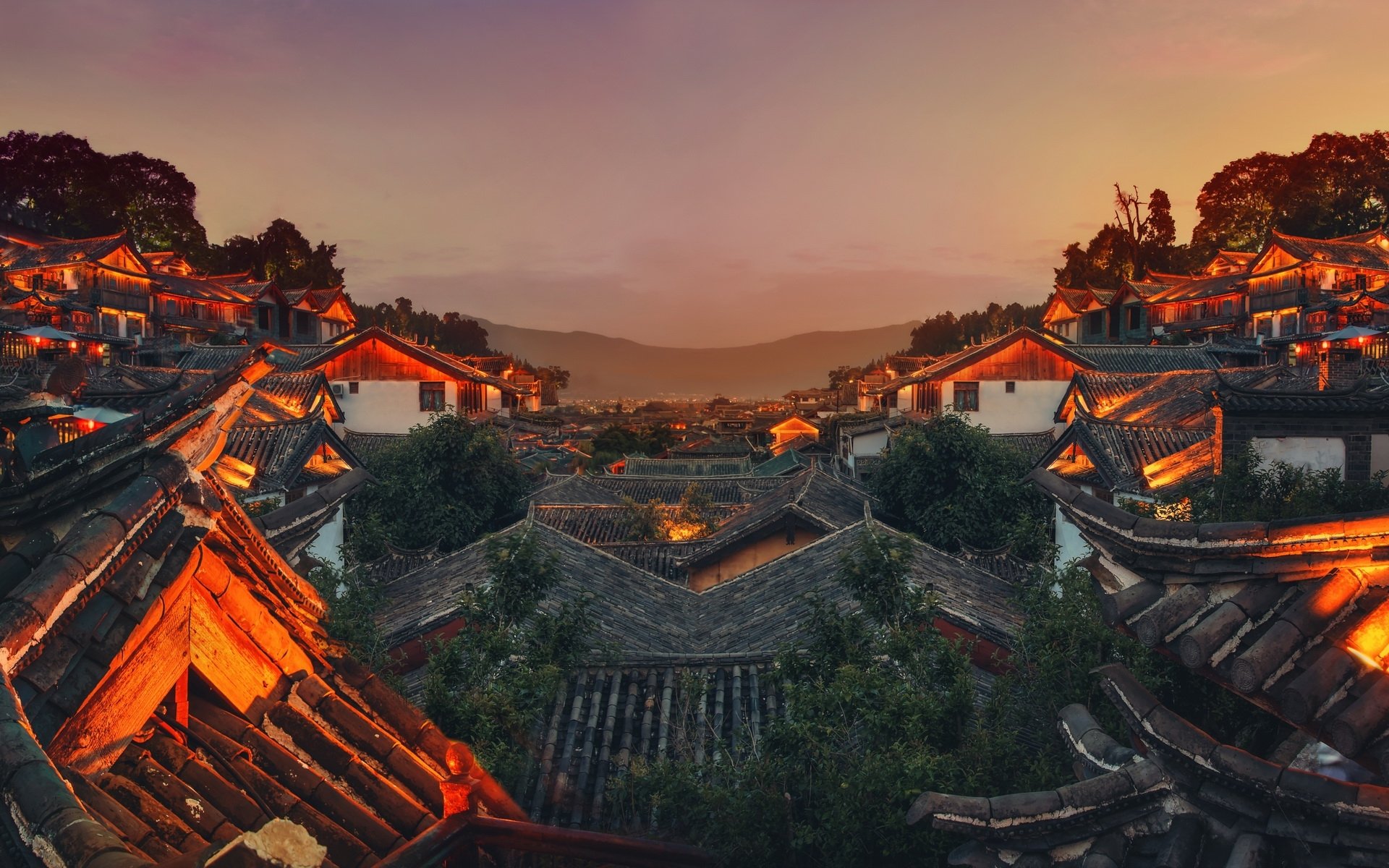 A panoramic view of traditional man-made buildings in Lijiang at dusk, illuminated by warm lights against a serene sky.
