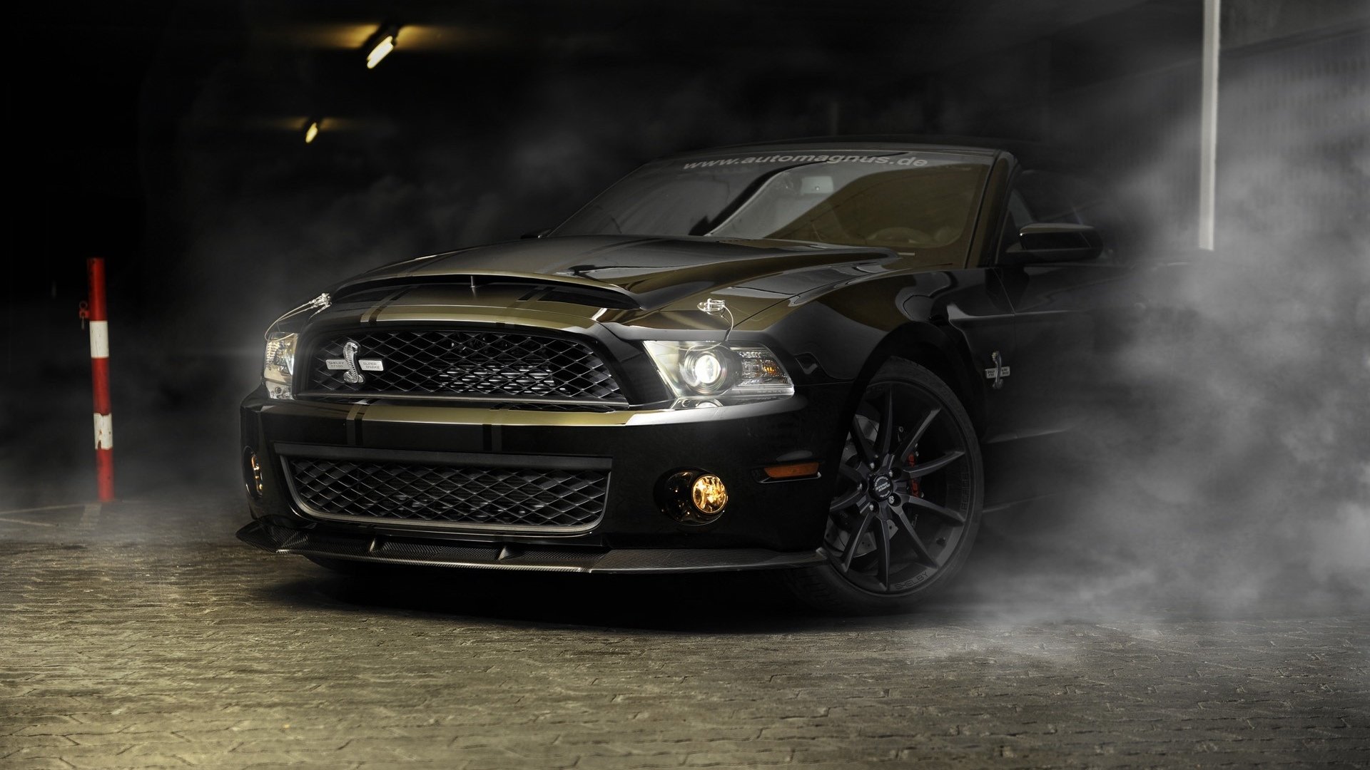 A black Ford Mustang Shelby Cobra GT 500 is parked in a dimly lit, foggy underground garage.