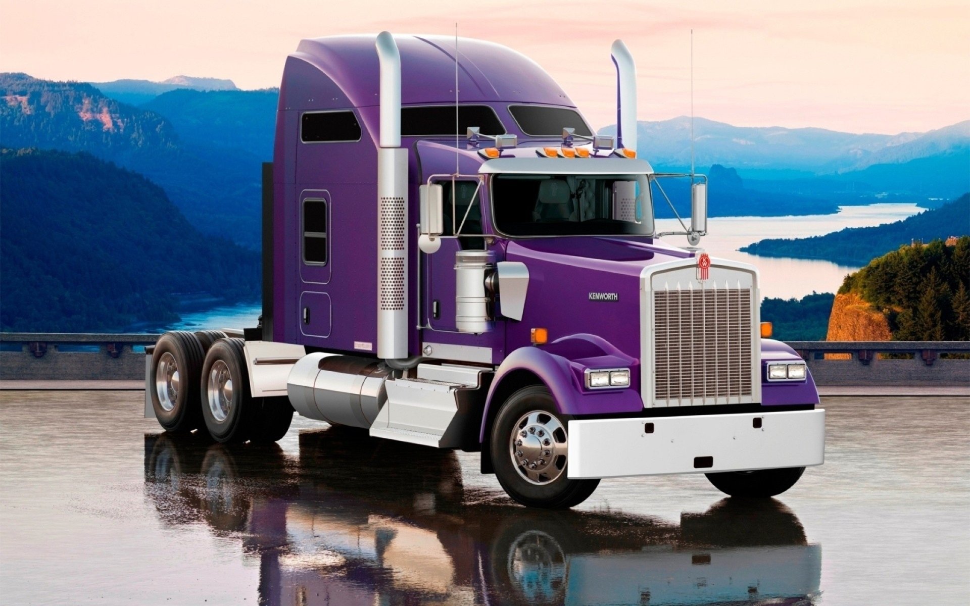 A purple Kenworth truck is parked on a wet surface with mountains and a lake in the background during sunset.