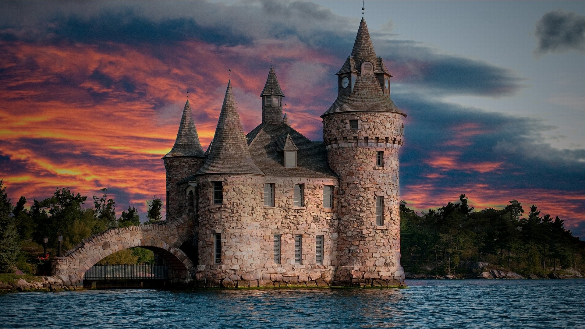 Boldt Castle, a man-made stone fortress with turrets, stands on an island surrounded by water under a vibrant, colorful sunset sky.