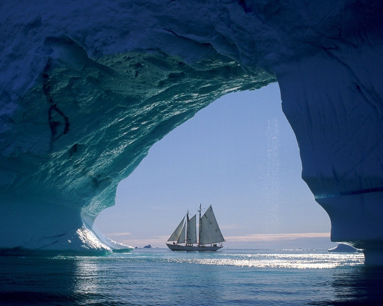 A majestic sailboat navigates through icy waters, framed by a dramatic ice arch, showcasing the stunning beauty of nature and marine exploration.