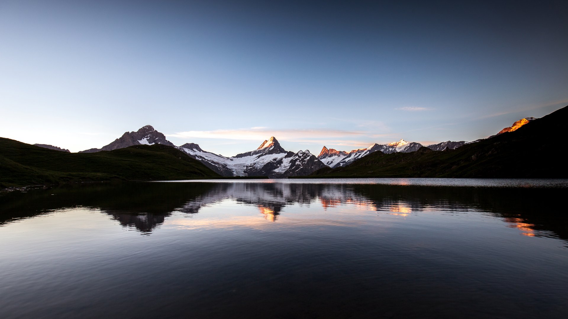Sunset over Lake Bachalpsee in Switzerland, with clear reflections of surrounding mountains and pristine natural landscape.