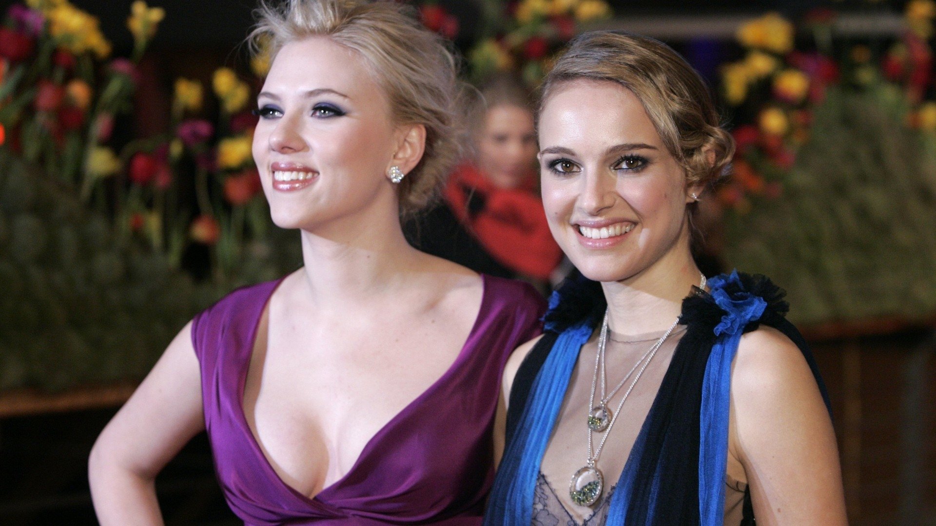 Scarlett Johansson and Natalie Portman, both talented actresses, pose together at an event surrounded by vibrant flowers, showcasing their elegant styles and celebrity charm.