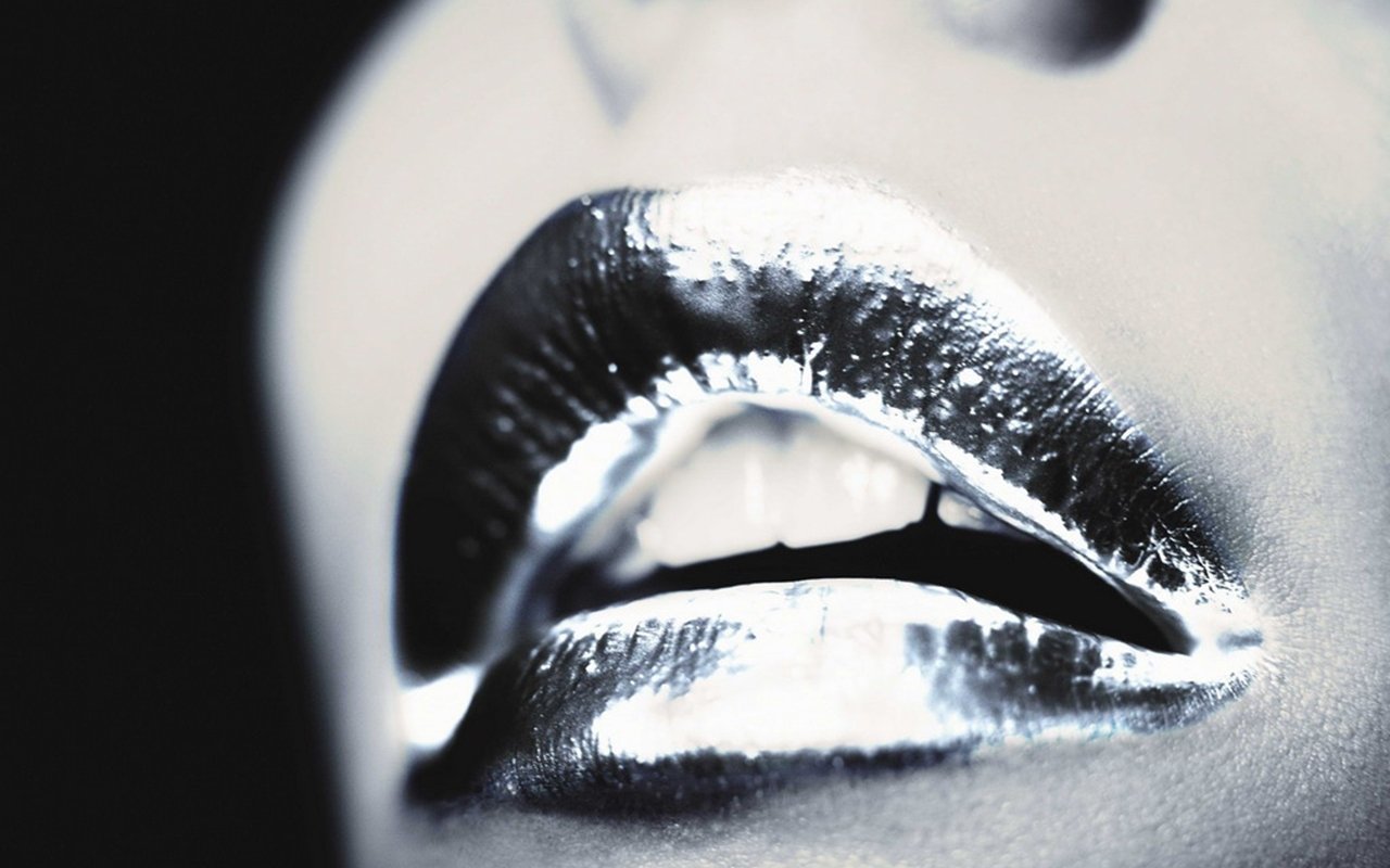 A close-up of a woman's lips, showcasing a striking metallic sheen. The image captures the glossy texture and shape, emphasizing a bold, artistic expression.