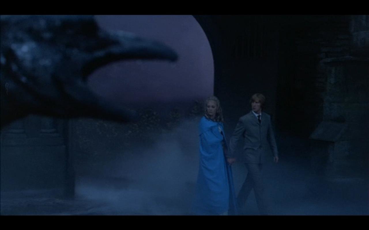 Wide shot from the movie Scars of Dracula: a monstrous claw reaches from the left foreground toward a man and woman walking through fog in a dark castle courtyard.
