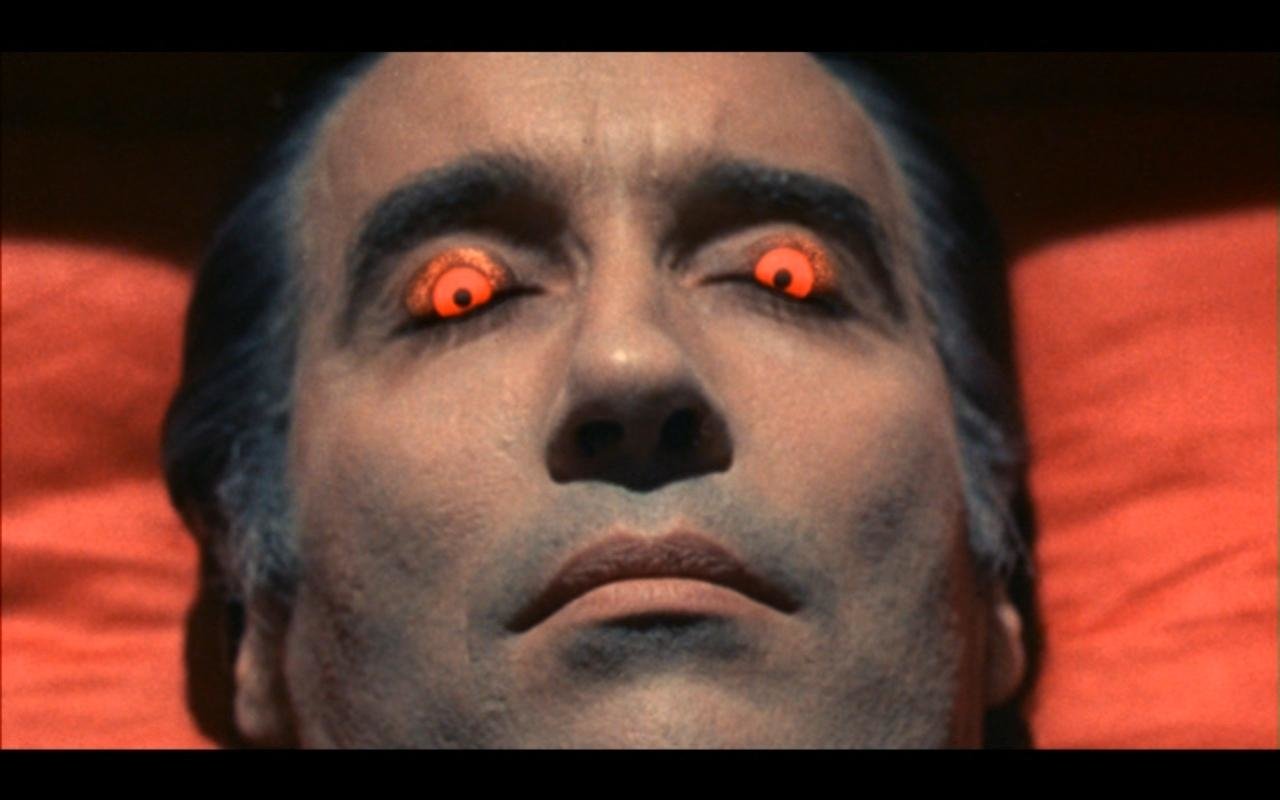 Close-up of a pale man with glowing red eyes lying back, a scene from the movie Scars of Dracula.