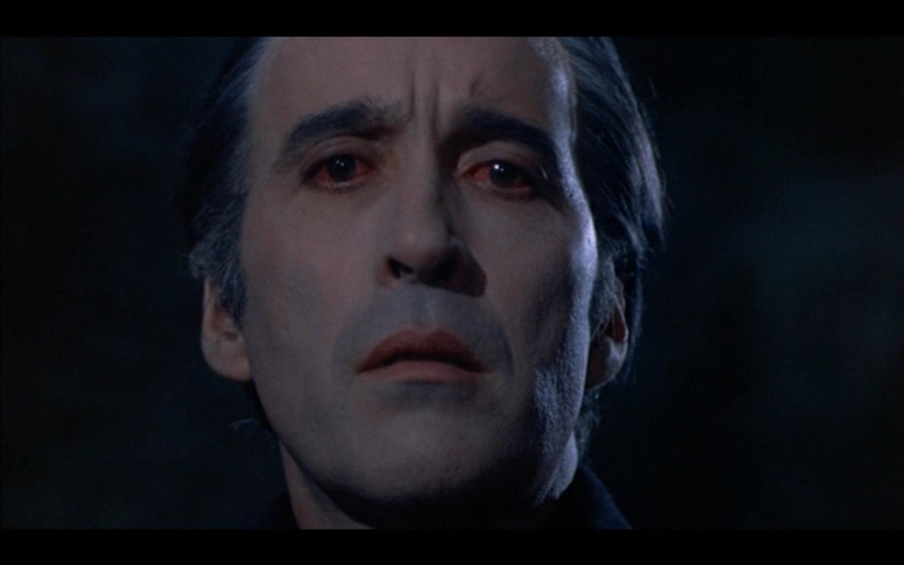 Close-up of a pale, intense man with red eyes from the movie Scars of Dracula, set against a dark, eerie background.