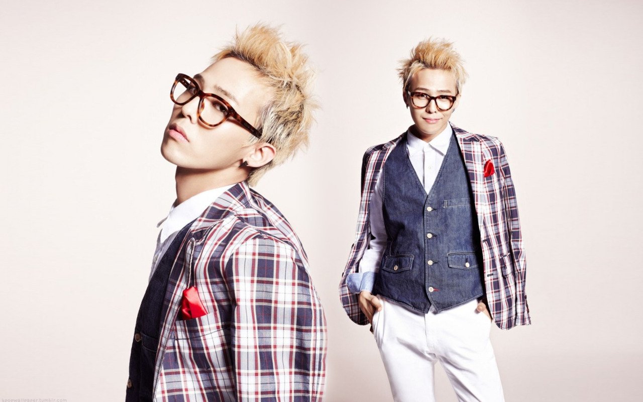 A stylish musician from Bigbang poses confidently in a plaid blazer and glasses, showcasing a trendy look with a playful attitude.