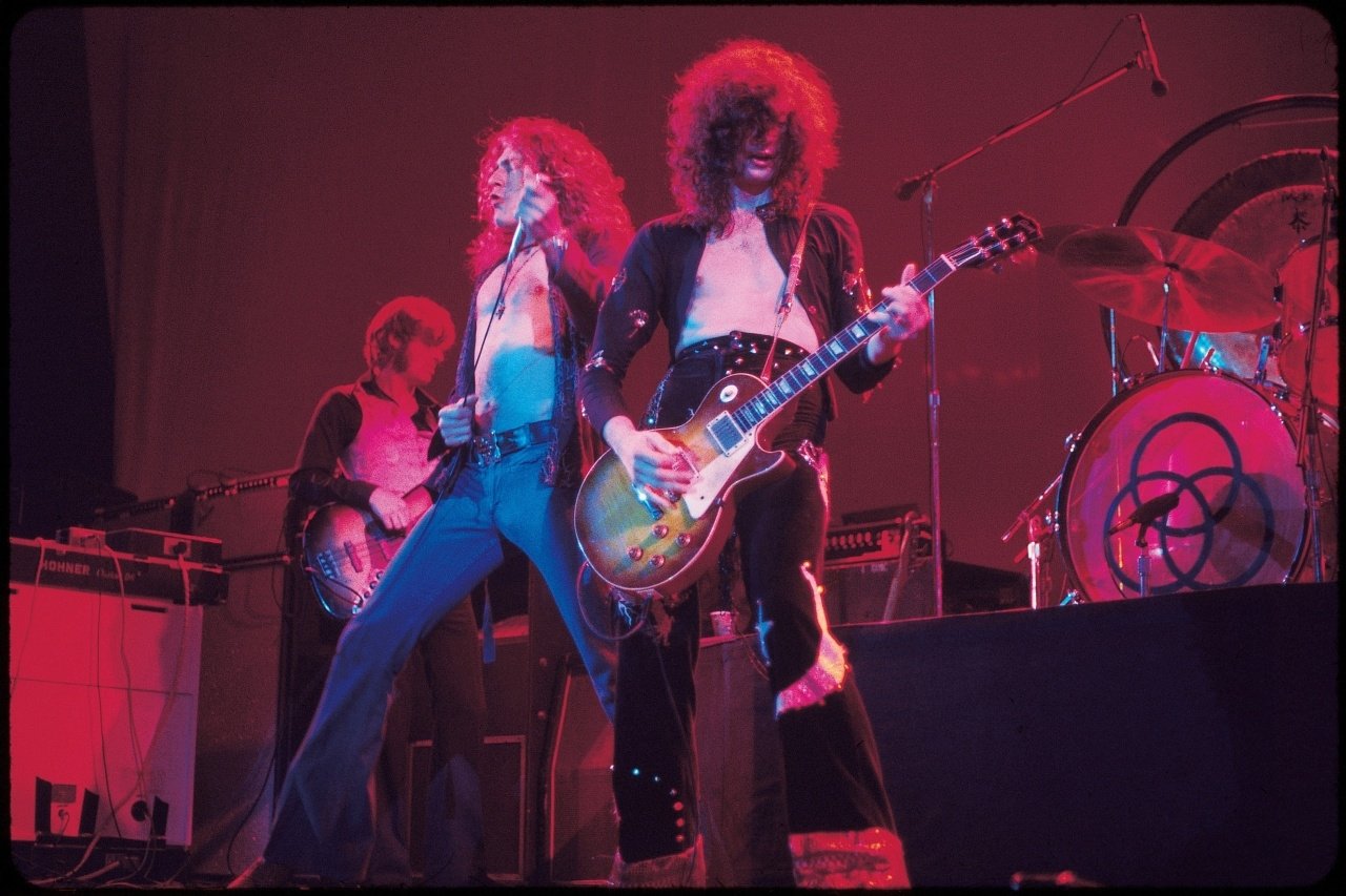 Two musicians perform energetically on stage, showcasing their vibrant outfits and instruments, celebrating the iconic sound of Led Zeppelin during a live concert.
