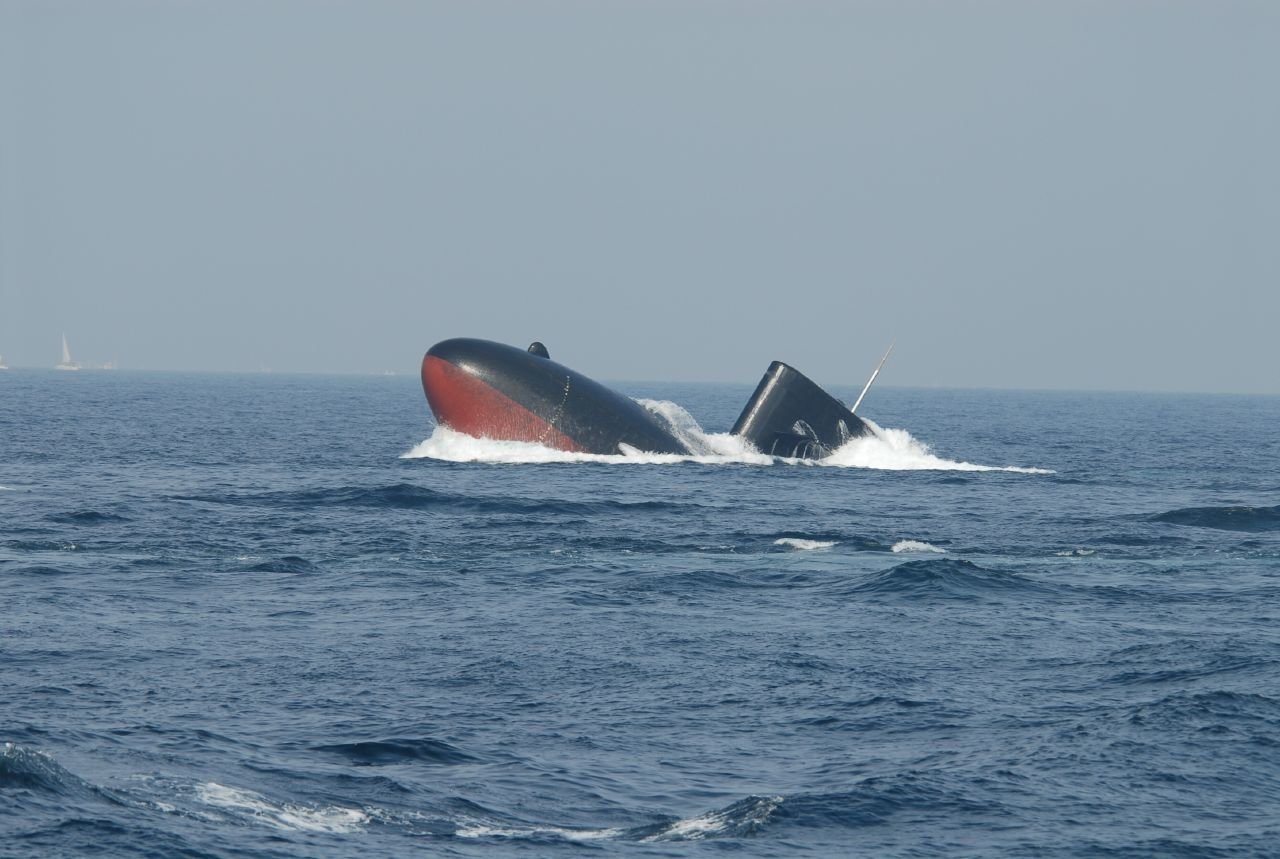 A military submarine partially breaches the water's surface, creating waves as it navigates through the ocean, showcasing its sleek design and operational capabilities.