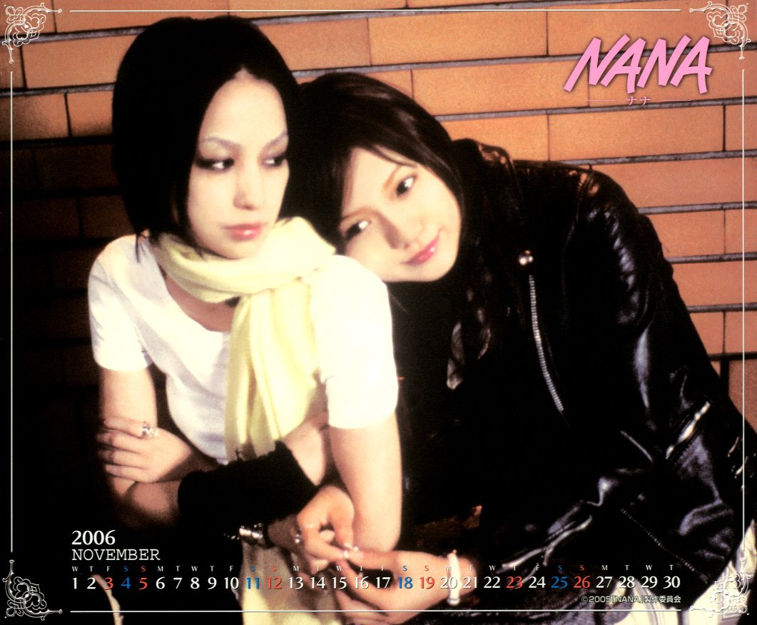 Nana Osaki from the movie Nana 2 sits against a brick wall with a friend; she wears a pale yellow scarf while the friend in a black leather jacket rests her head on Nana's shoulder.