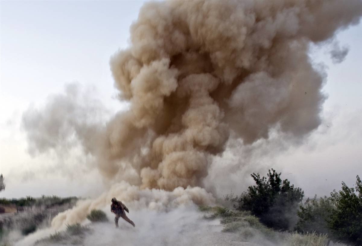 A military figure moves quickly away from a large explosion, creating a dramatic cloud of dust and smoke in the air, emphasizing the intensity of the scene.